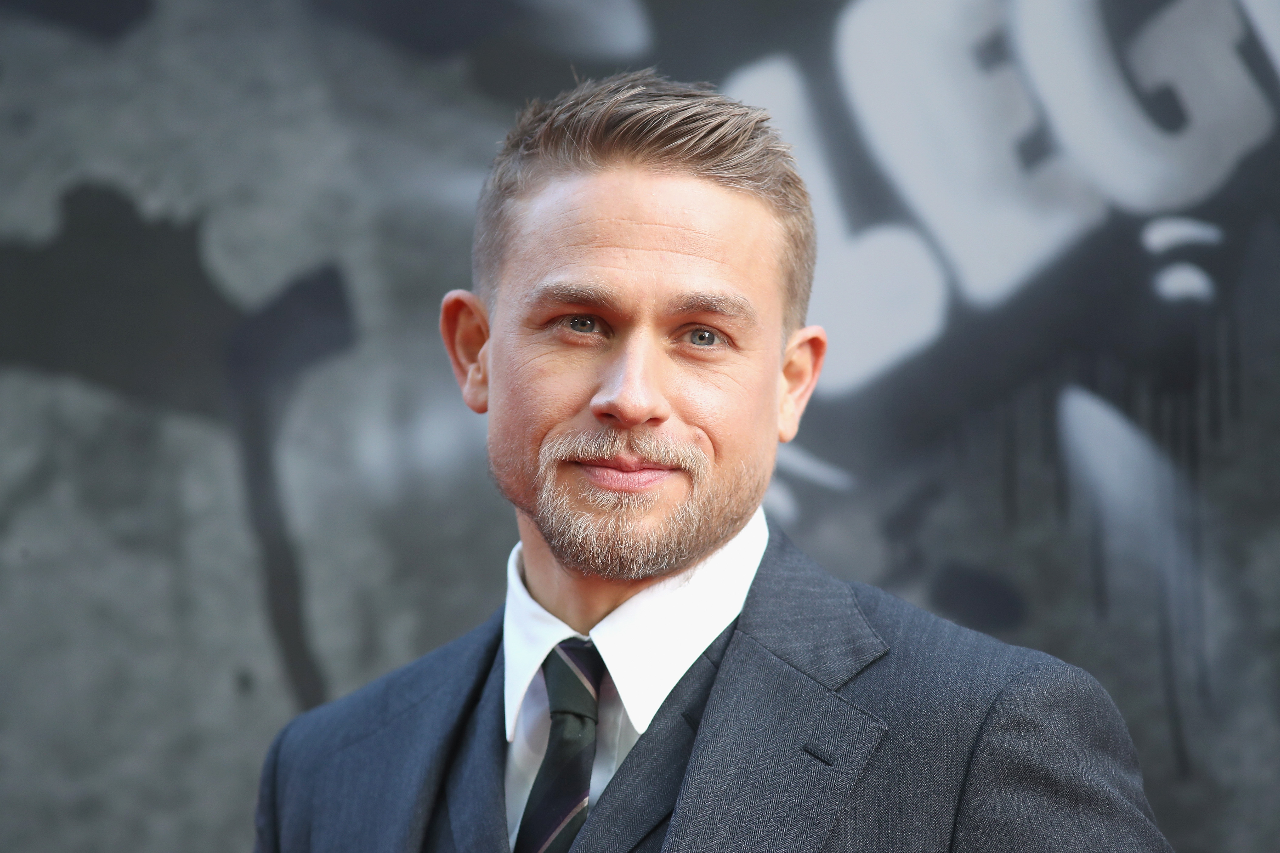 Charlie Hunnam smiles for a photo wearing a suit and tie at theEuropean premiere of 'King Arthur: Legend of the Sword'.