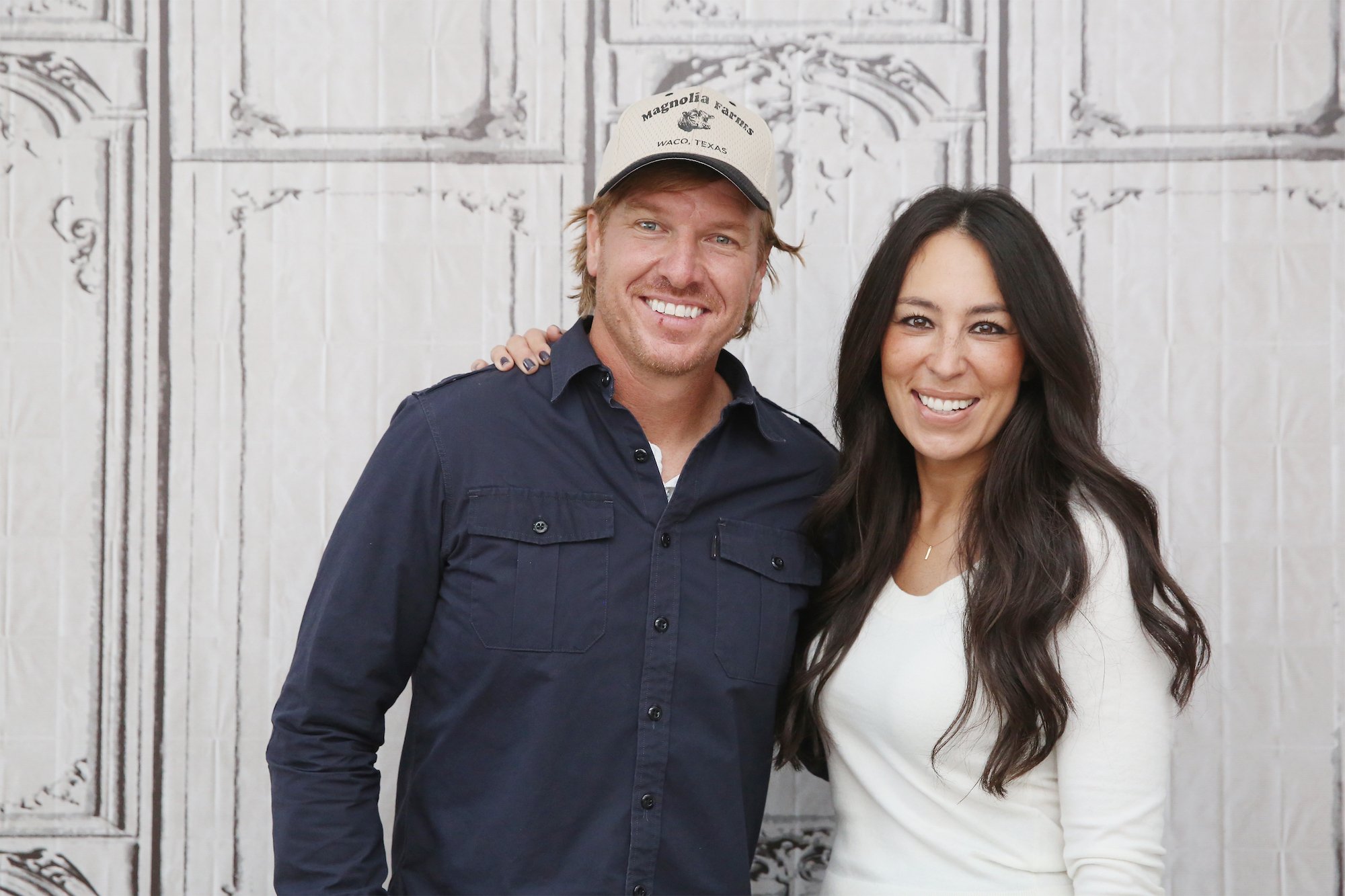 Chip and Joanna Gaines smile at an AOL event, with Chip wearing a dark button down shirt and hat and Joanna wearing a white top.
