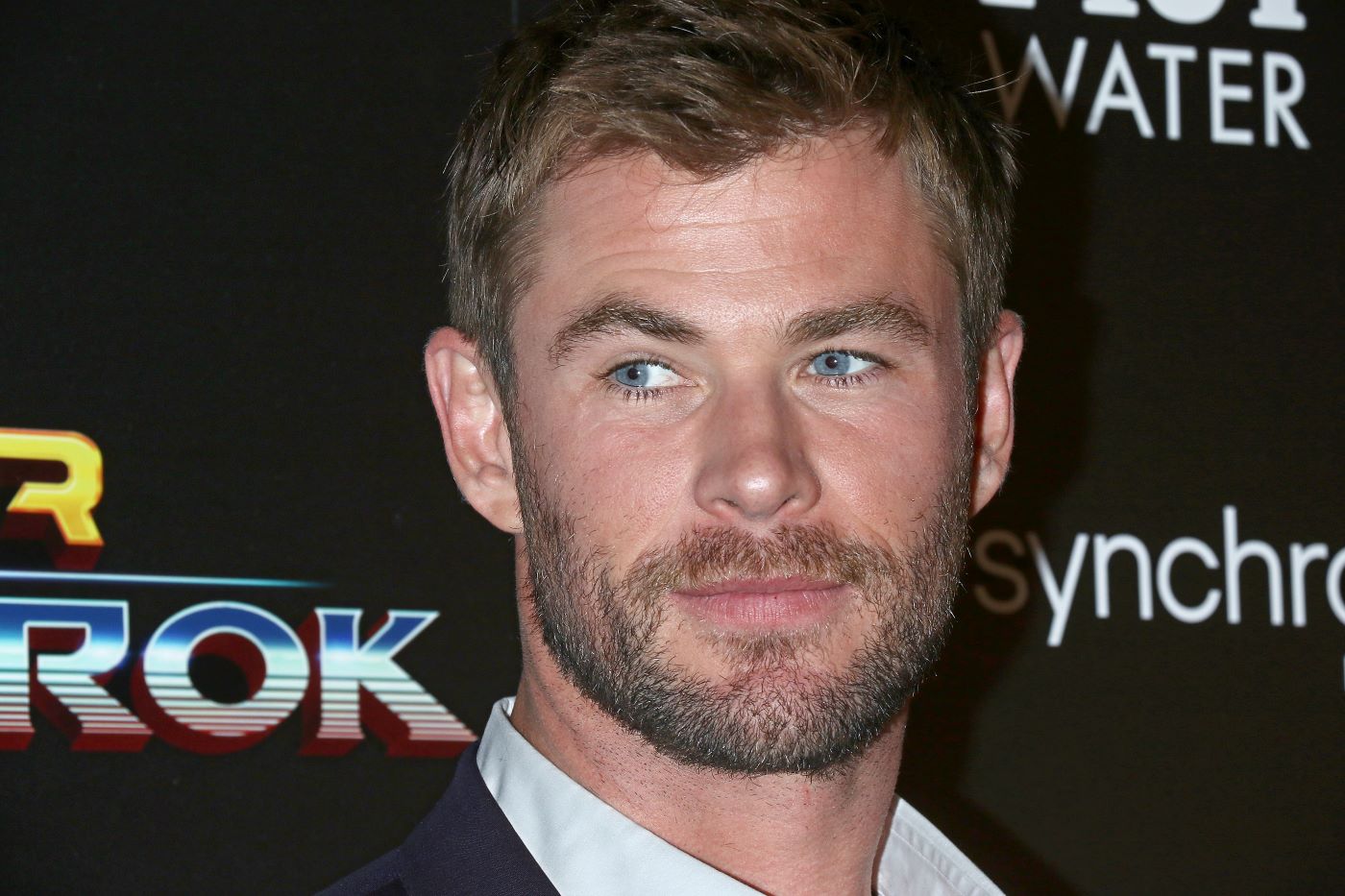 Chris Hemsworth dressed in a white collared shirt and a black background.