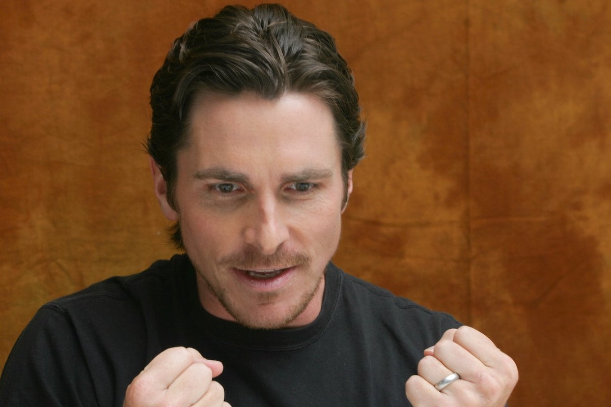 Christian Bale looks down and balls up his fists amid a brown background