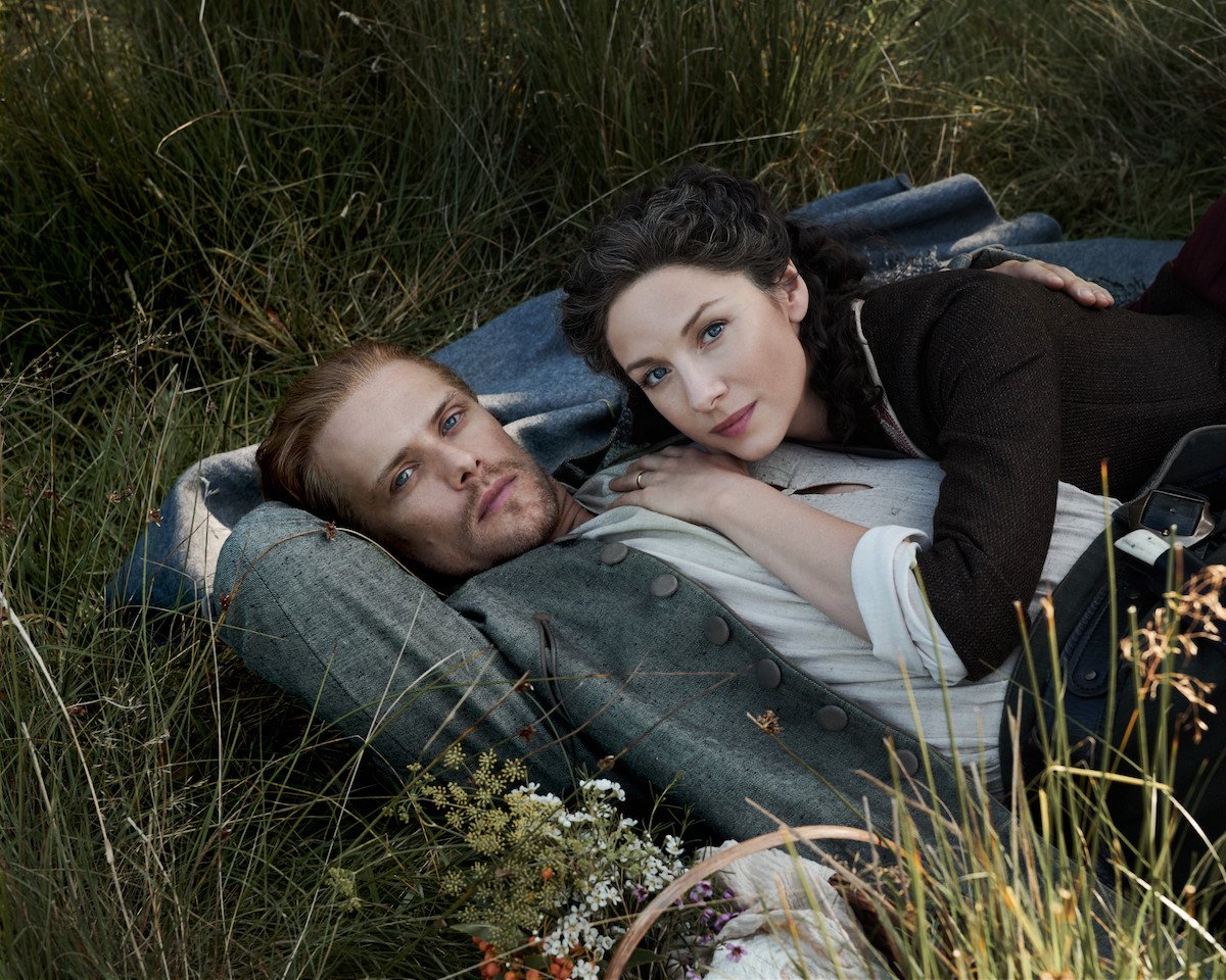 Sam Heughan and Caitriona Balfe as Jamie and Claire Fraser from 'Outlander' lying in the grass. The 'Outlander' Season 6 sex scenes were able to be included due to STARZ's strict COVID-19 safety rules, but Heughan says the scenes brought about new acting challenges for him and Balfe.