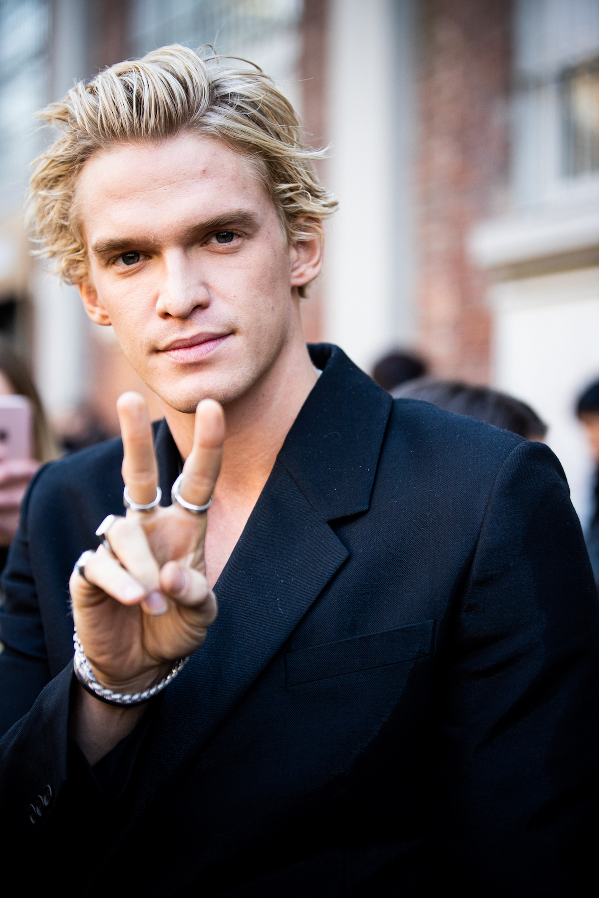 Cody Simpson in a black jacket smiles and flashes a peace sign at the camera.