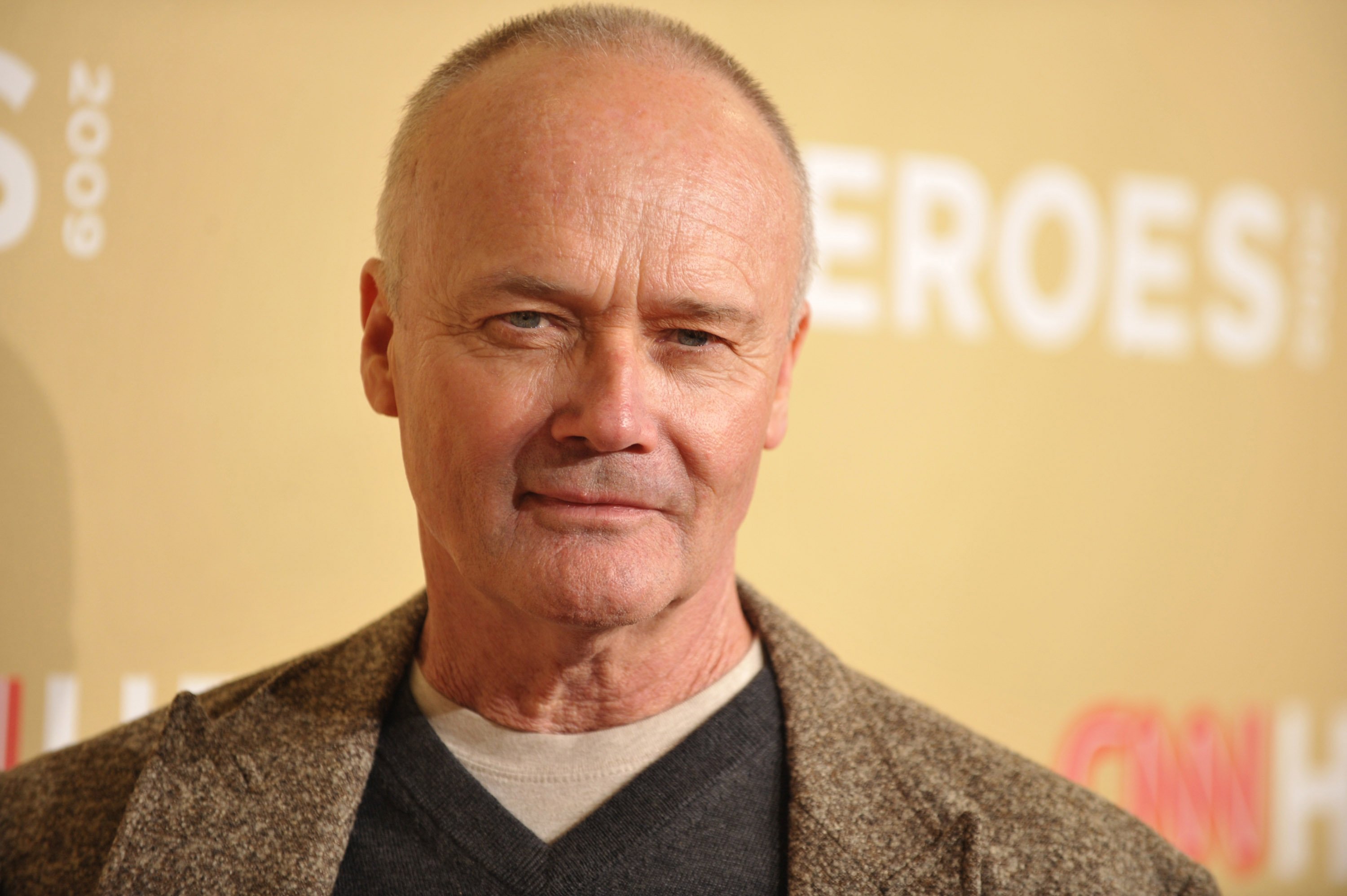 Creed Bratton from 'The Office' standing in front of a yellow backdrop wearing a brown jacket and navy shirt at the 2009 CNN Heroes Awards.