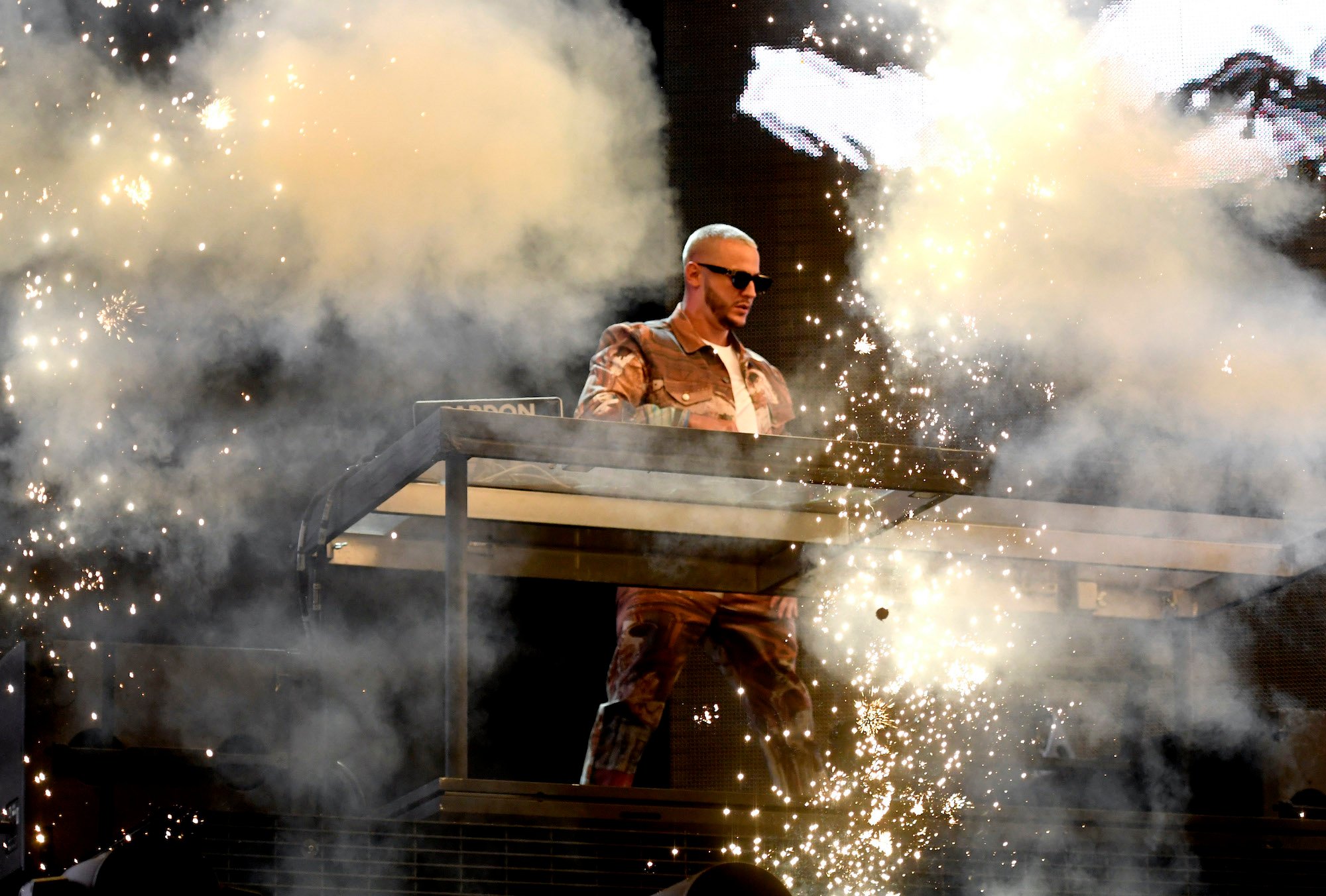 DJ Snake performing on stage with smoke and firework effects in foreground