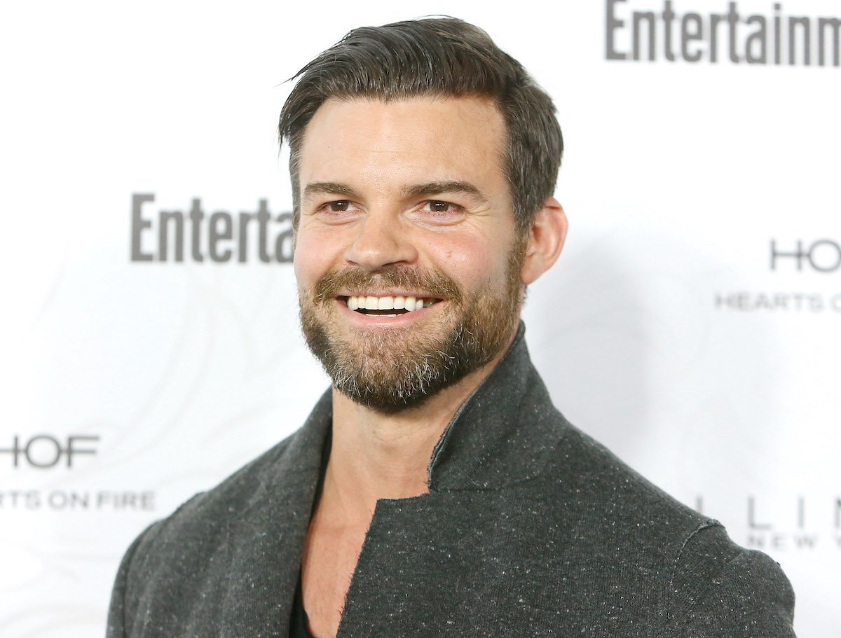 Daniel Gillies smiles on the red carpet wearing a grey jacket