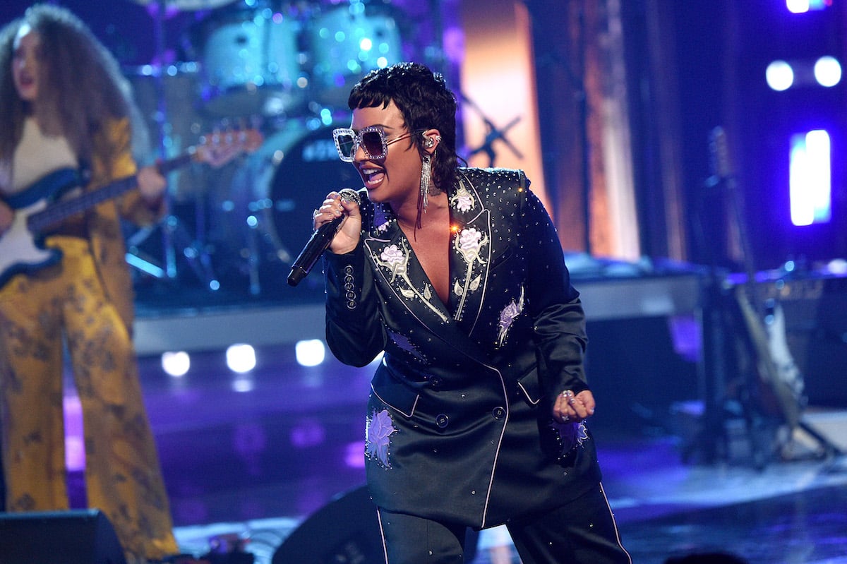 Demi Lovato singing onstage wearing a suit and sunglasses.