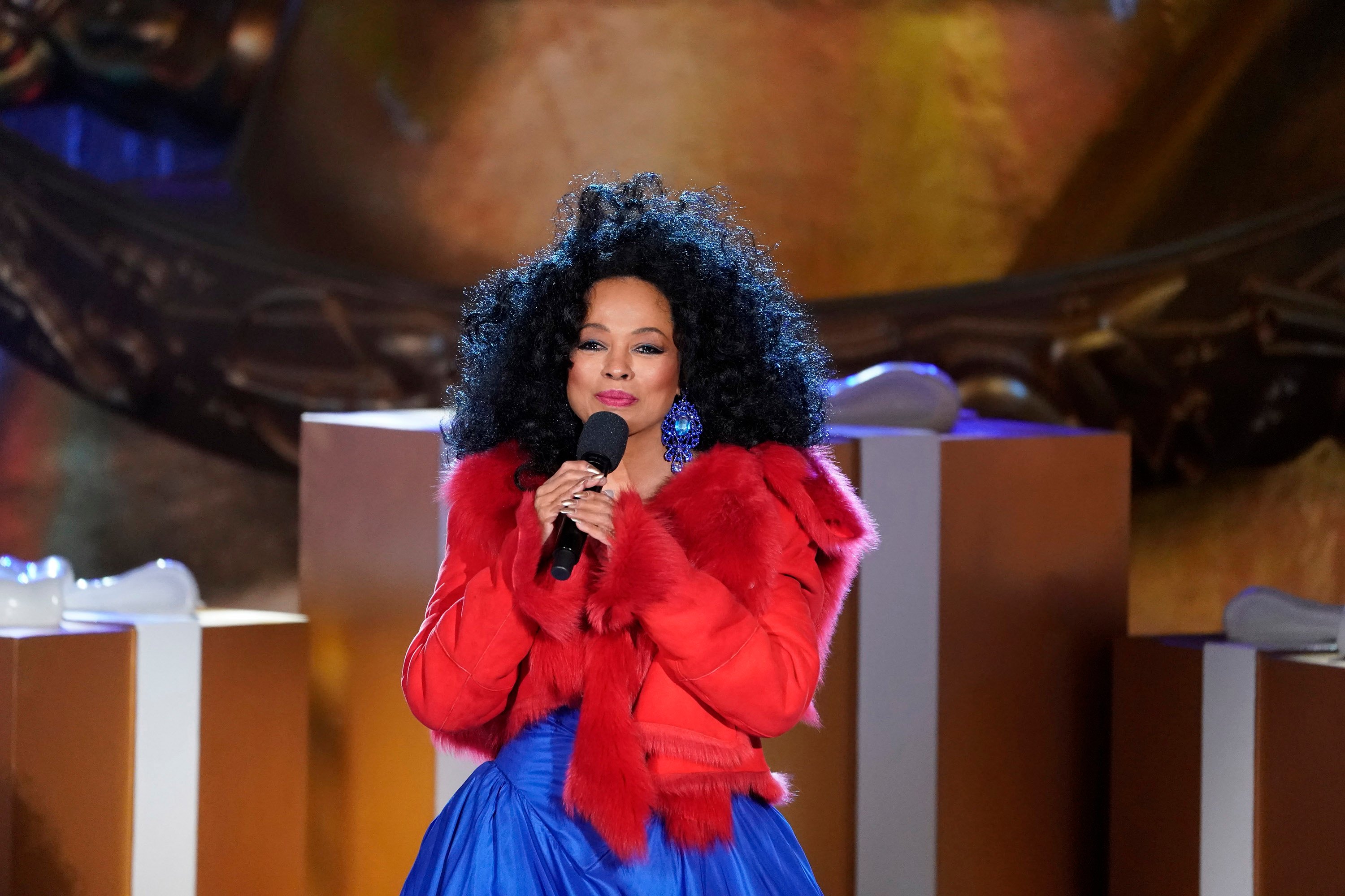 Diana Ross wearing a blue dress and red jacket while singing.
