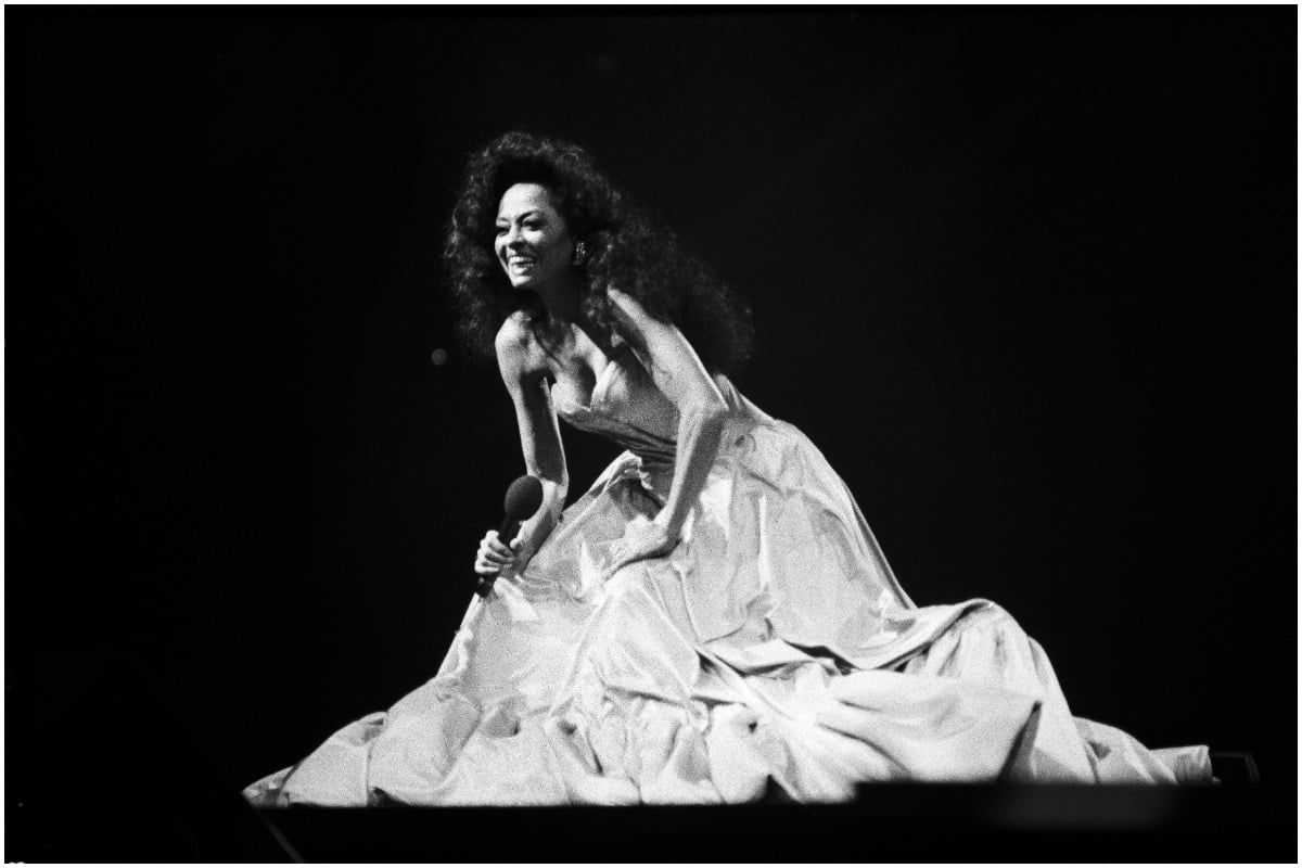 Diana Ross kneeling down and singing in a black and white photo.