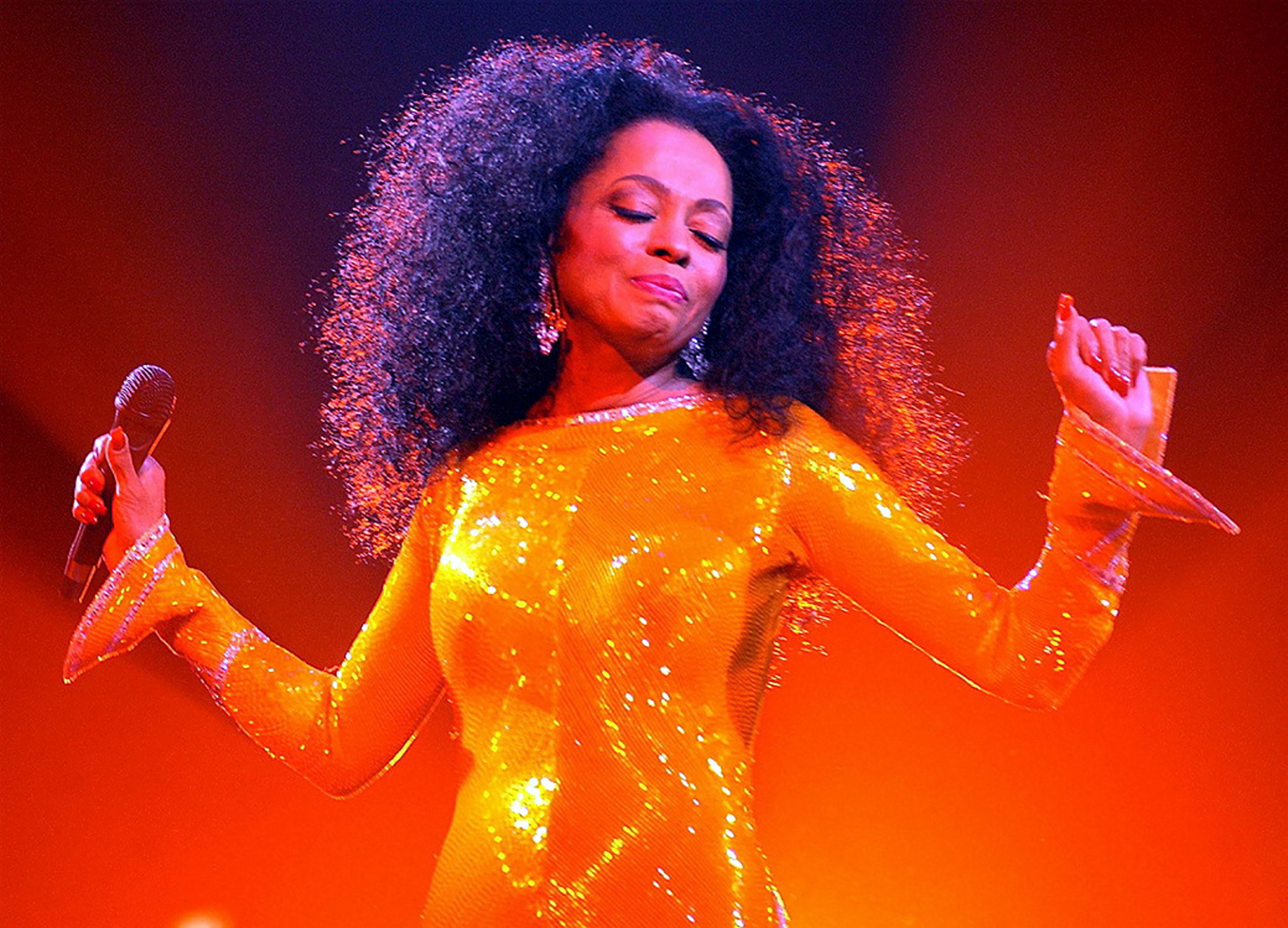 Diana Ross performing onstage in an orange sequined gown.