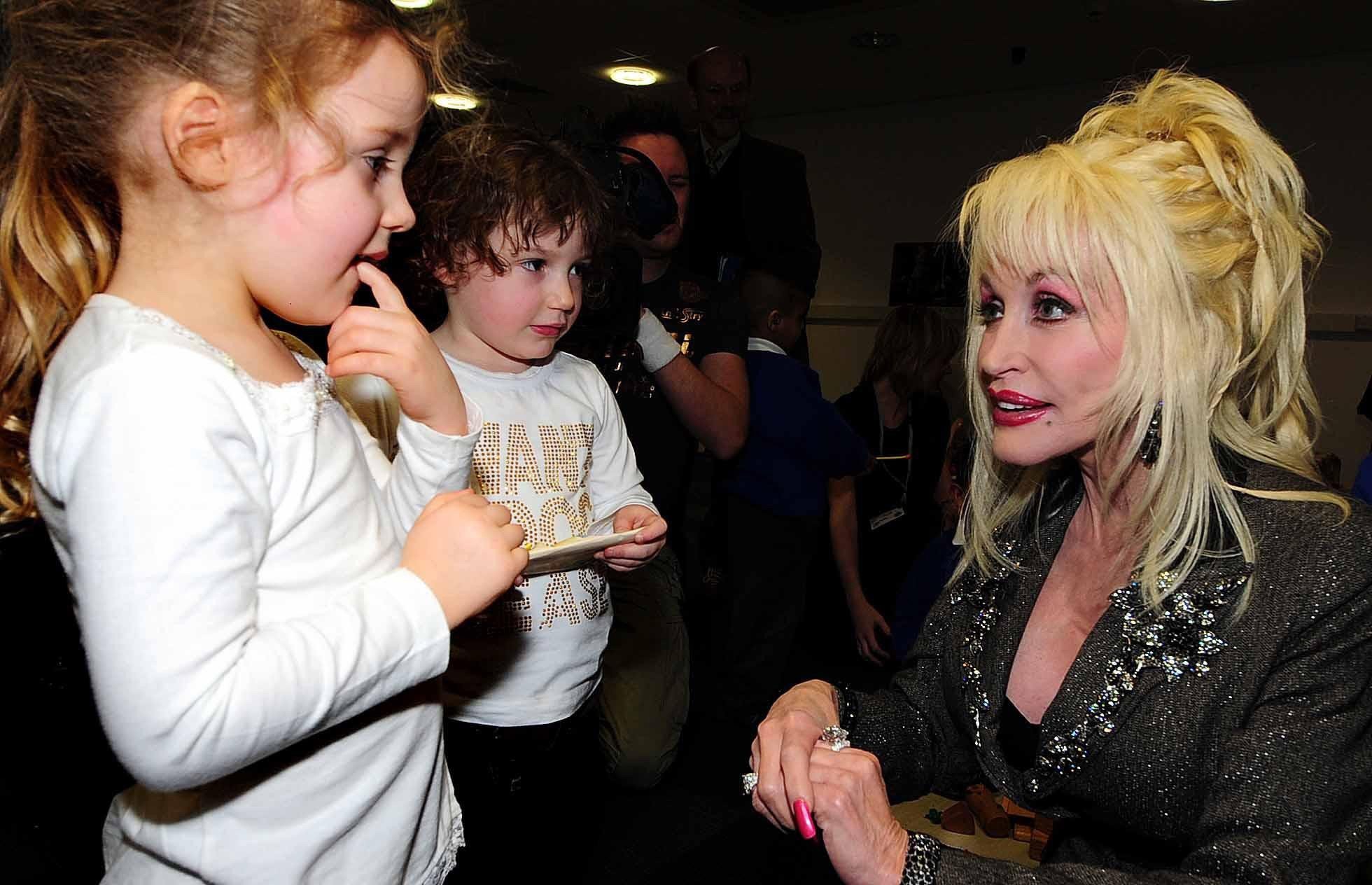 Dolly Parton crouches down to speak with two children.