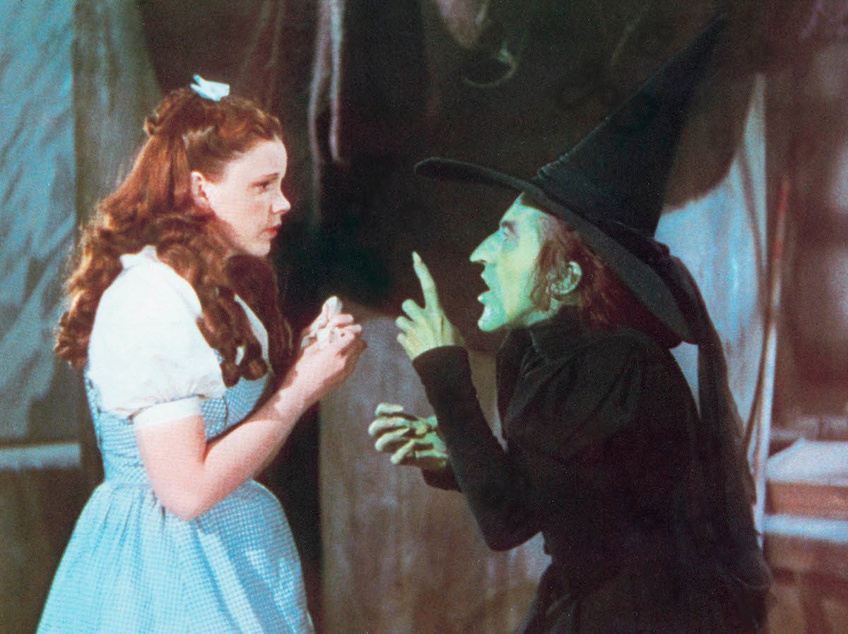Judy Garland cowers as Margaret Hamilton holds up a hand threateningly in ‘The Wizard of Oz’