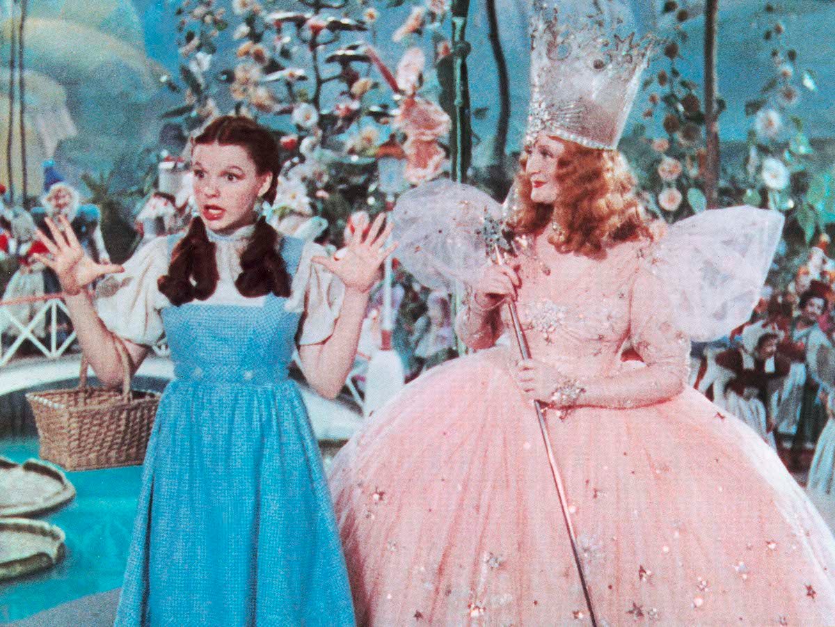 Judy Garland raises her hands while speaking as a smiling Billie Burke looks on in ‘The Wizard of Oz’