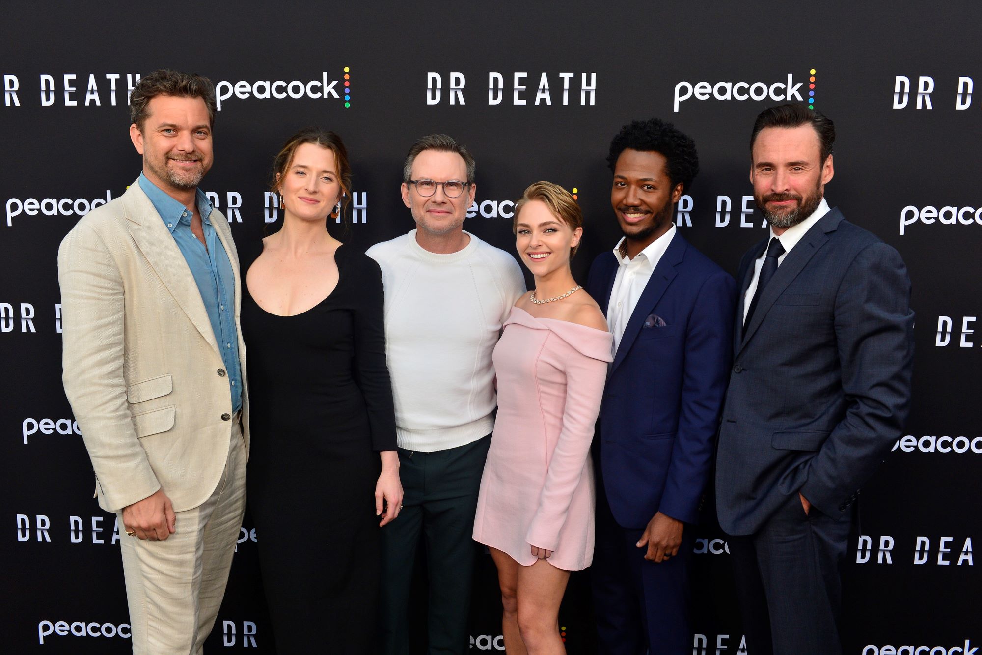 Six members of the cast of Dr. Death professionally dressed standing in front of a black background with Dr. Death and peacock written on it.