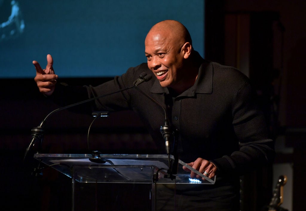 Dr. Dre speaks on stage at a Grammy event. He's dressed in all black.