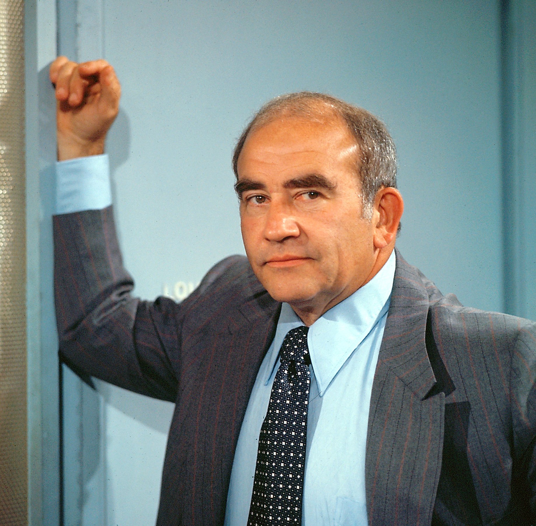 Ed Asner as Lou Grant leans on a door