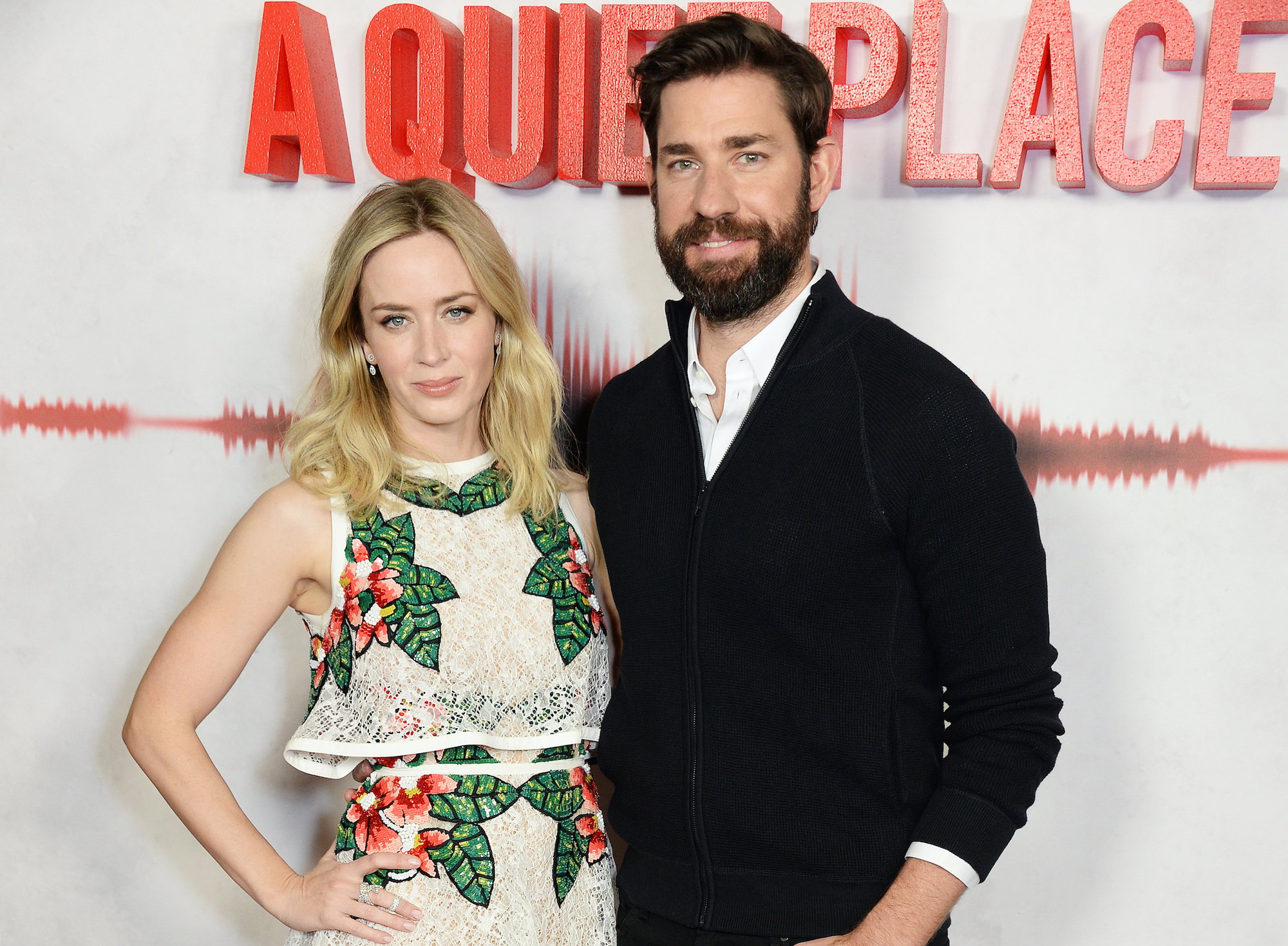 Emily Blunt and John Krasinski smiling in front of a background with the 'A Quiet Place' logo