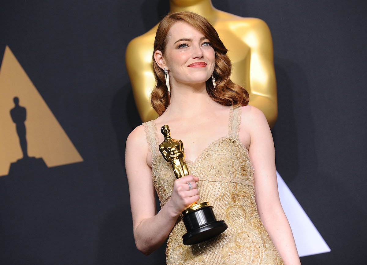 Emma Stone smiles and poses while holding her Oscar