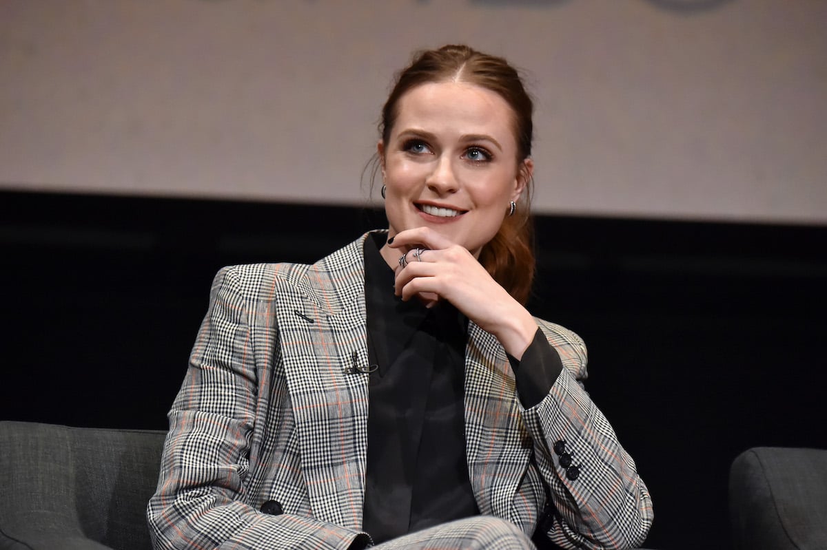 Evan Rachel Wood wearing a suit, sitting down and smiling with her hand on her chin.
