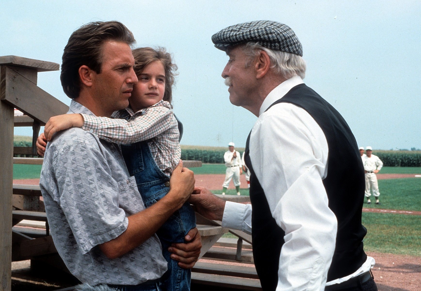 Kevin Costner holds Gaby Hoffmann while talking to Burt Lancaster in front of the field in 'Field of Dreams' in 1989