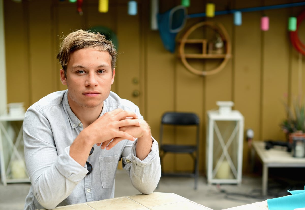 Finn Cole in a grey button-down sitting with his hands folded on a table.