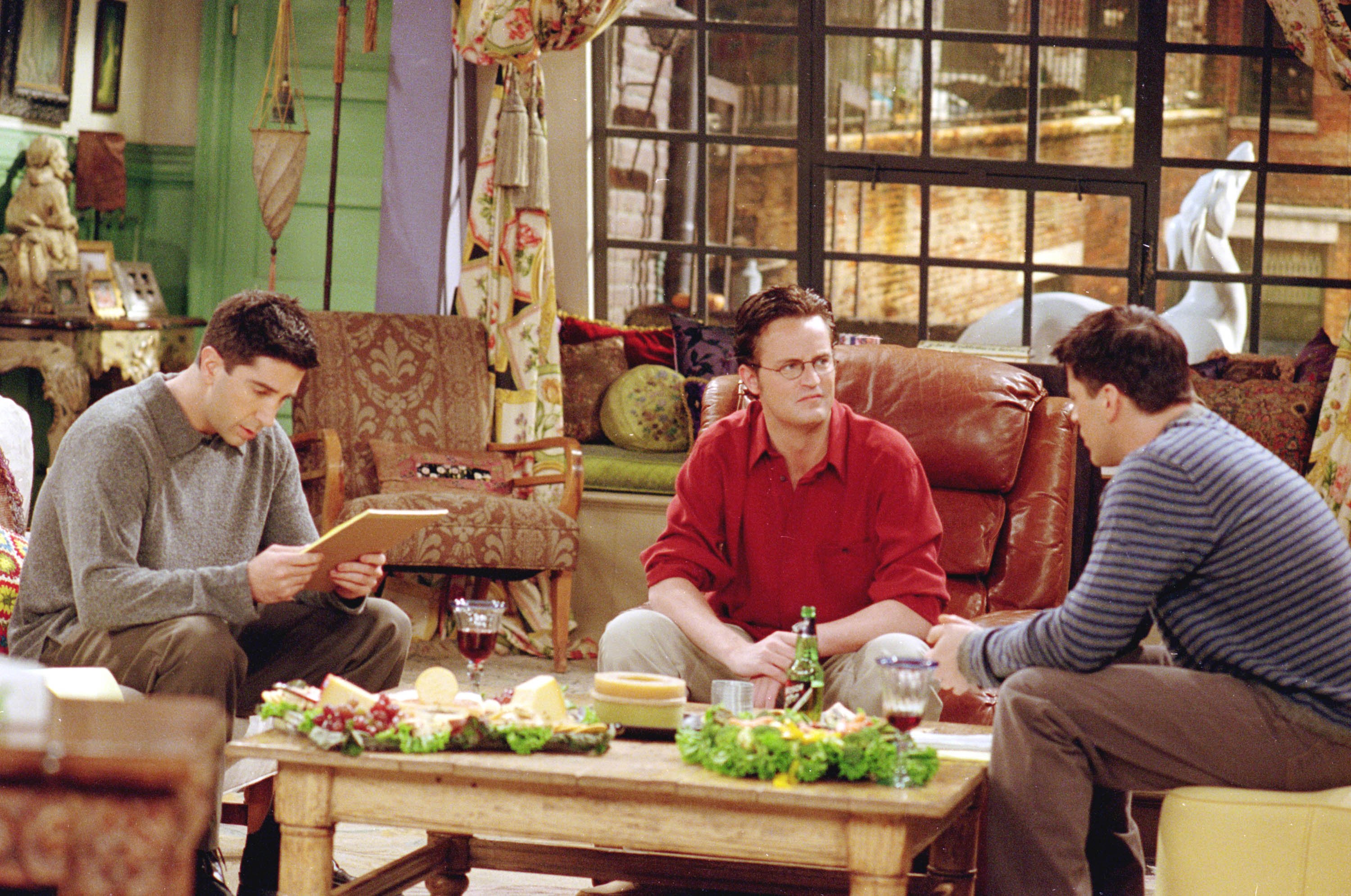 Ross Geller, Chandler Bing and Joey Tribbiani chat while sitting in the living room of Monica's apartment during a scene in 'Friends'
