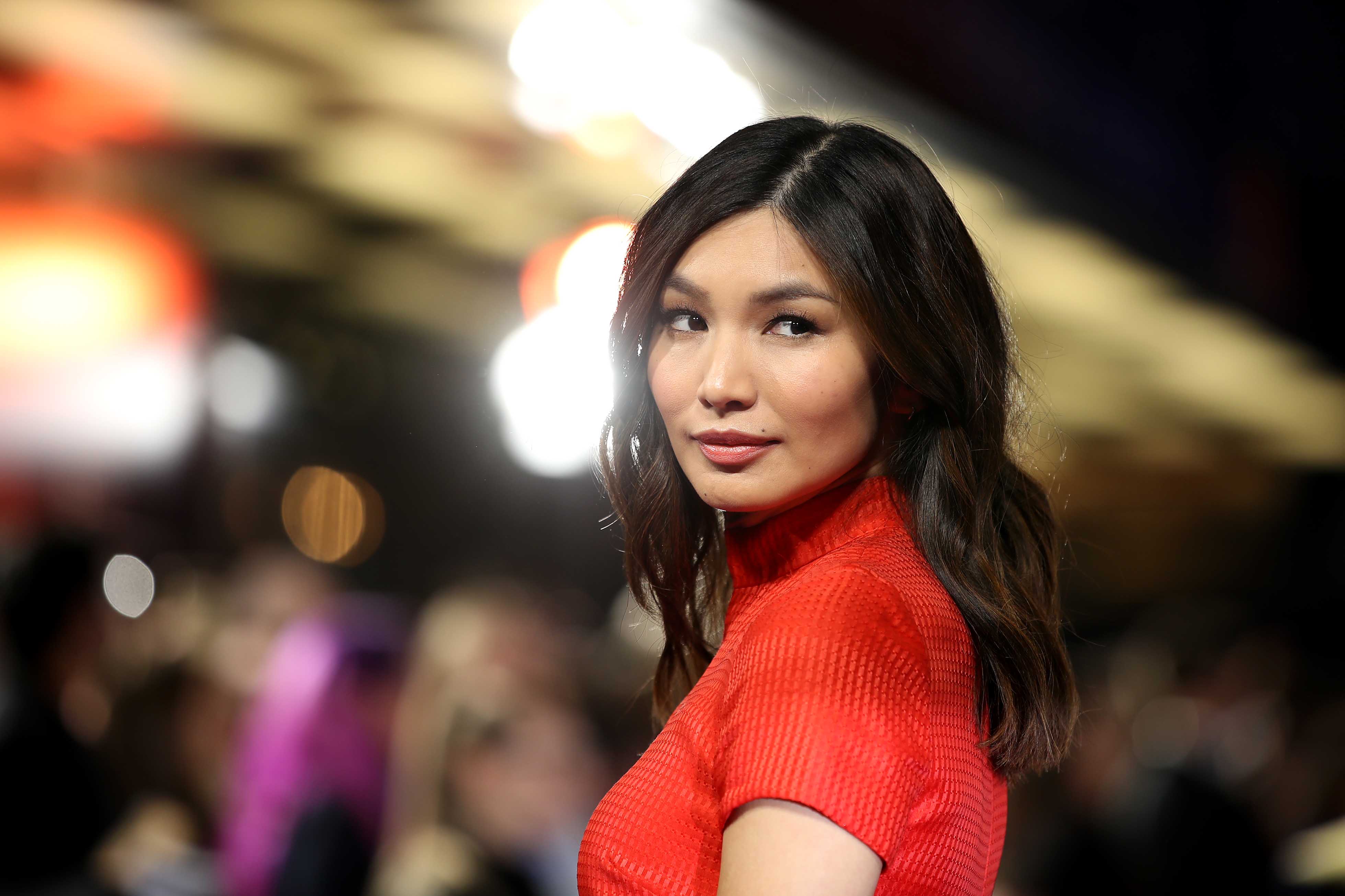 ‘Eternals’ star Gemma Chan from the chest up wearing a red top and looking over her left shoulder.