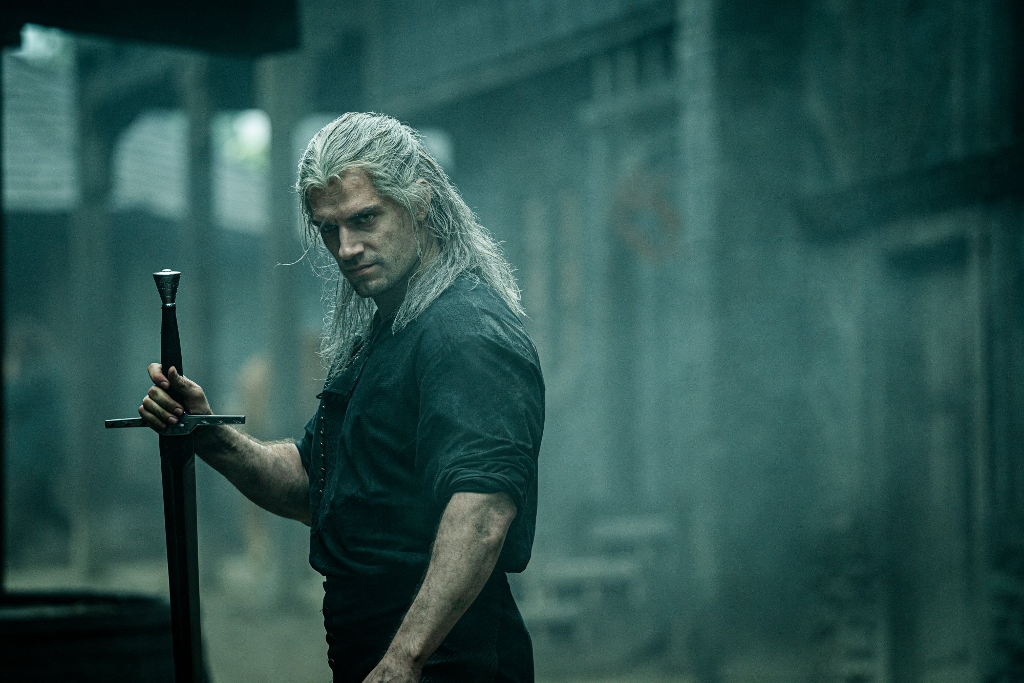 Henry Cavill as Geralt of Rivia on The Witcher. He's wearing a black tunic, holding a sword, and glaring at someone.