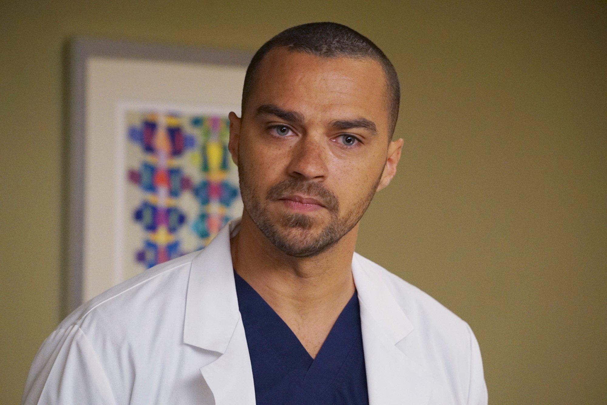 Jesse Williams as Jackson Avery on ABC drama 'Grey's Anatomy.' He's wearing dark blue scrubs and a white medical coat.