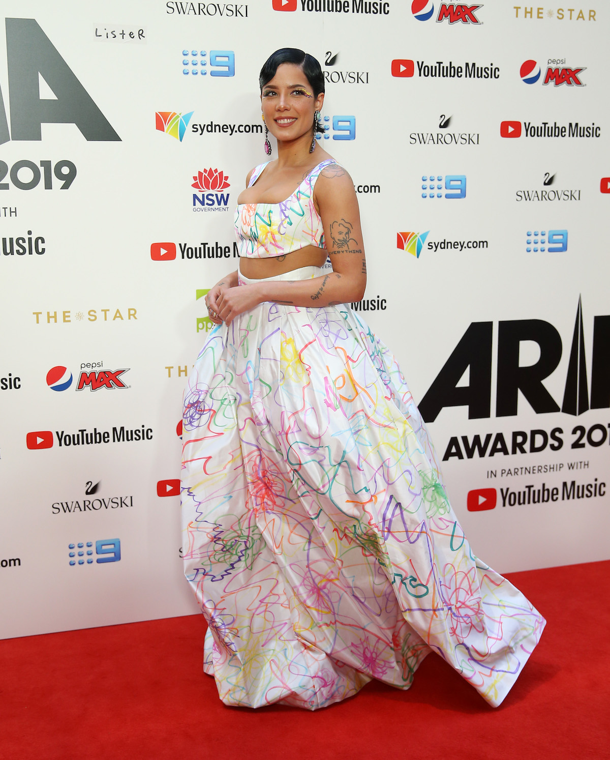 Halsey walks the red carpet in a long white gown covered in colorful designs.