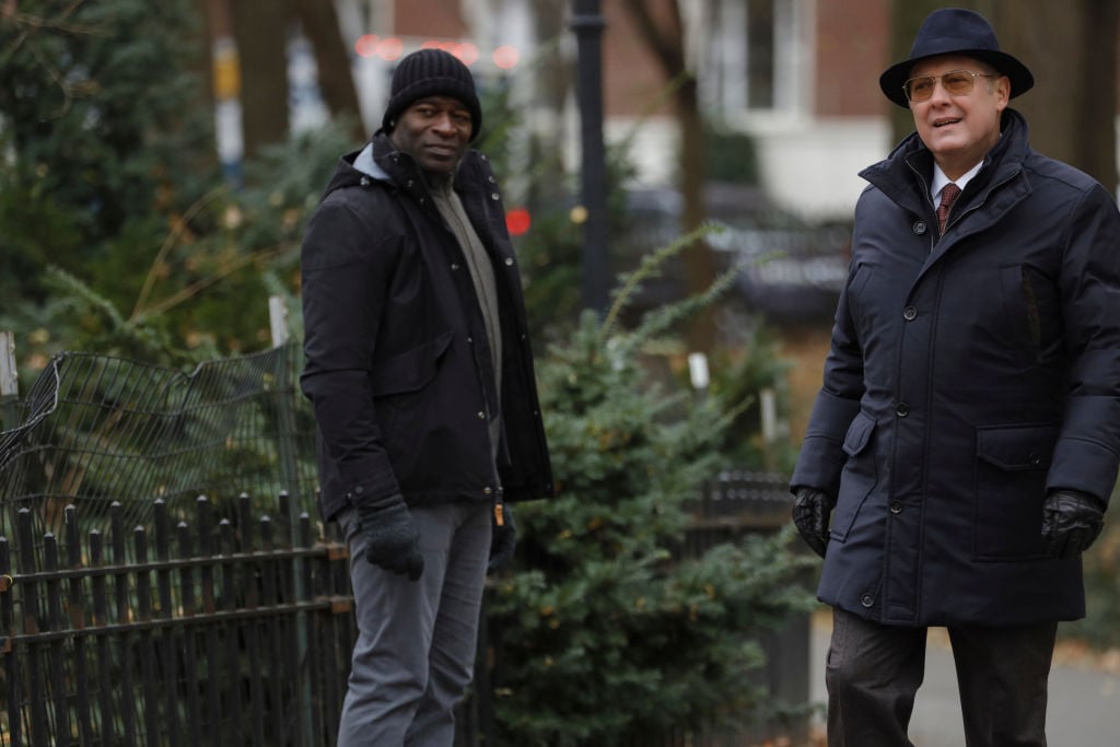Hisham Tawfiq as Dembe Zuma, James Spader as Raymond 'Red' Reddington stand outside. Both are dressed in winter gear.