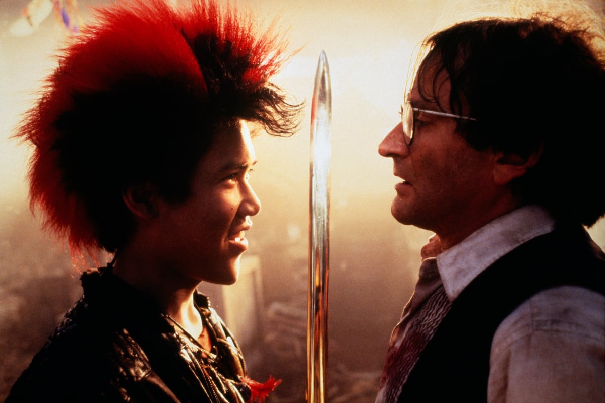 Dante Basco holds up a sword and smiles in front of Robin Williams in ‘Hook’