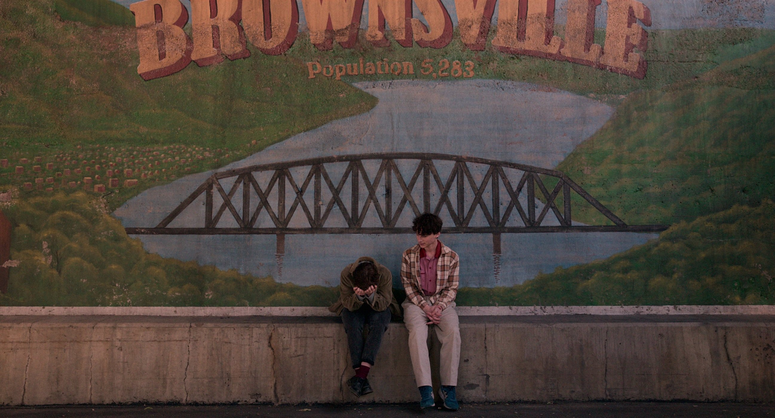 Sophia Lillis as Sydney Novak and Wyatt Oleff as Stanley Barber sit in front of the Brownsville sign in 'I Am Not Okay With This'