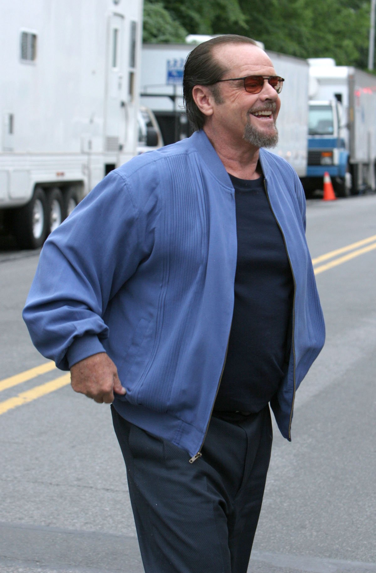 Jack Nicholson smiles wearing sunglasses, jeans, and a blue jacket on location for 'The Departed' in 2005