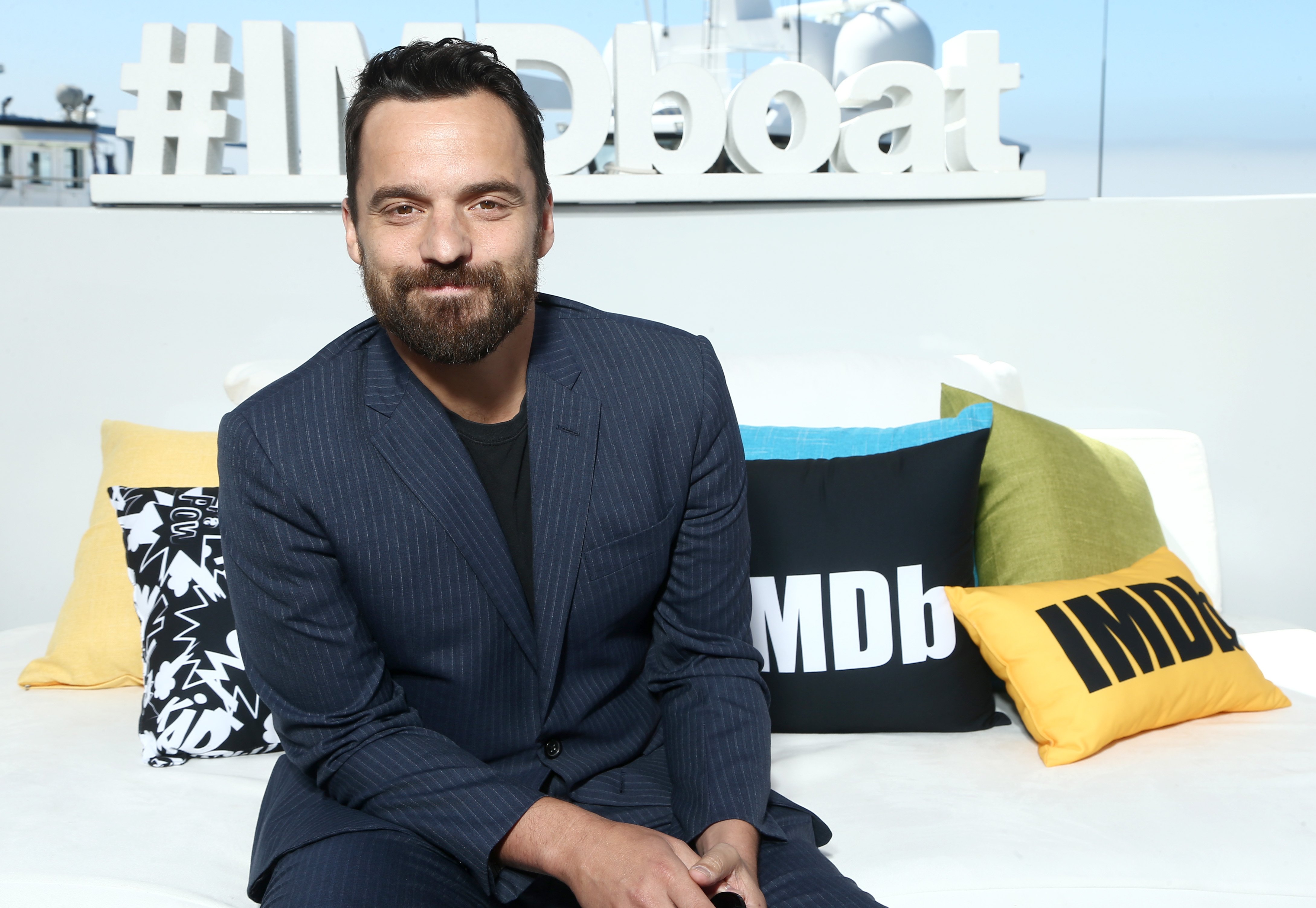 Jake Johnson smiles in front of imbd sign and pillows