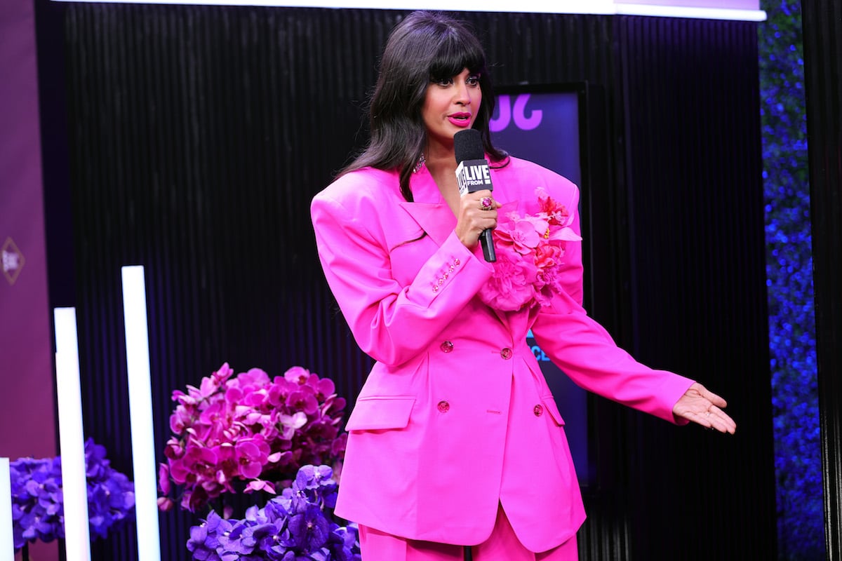 ameela Jamil at the 2020 E! People's Choice Awards wearing a pink suit and speaking into a microphone
