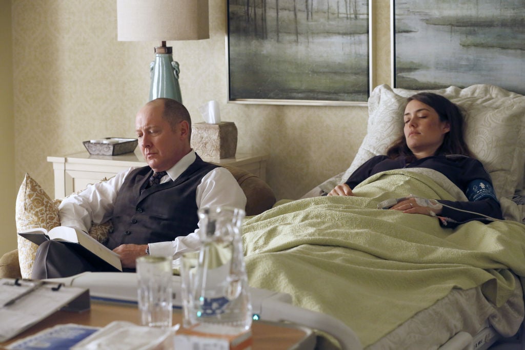 James Spader as Raymond 'Red' Reddington sits next to a hospitalized and sleeping Megan Boone as Elizabeth Keen.