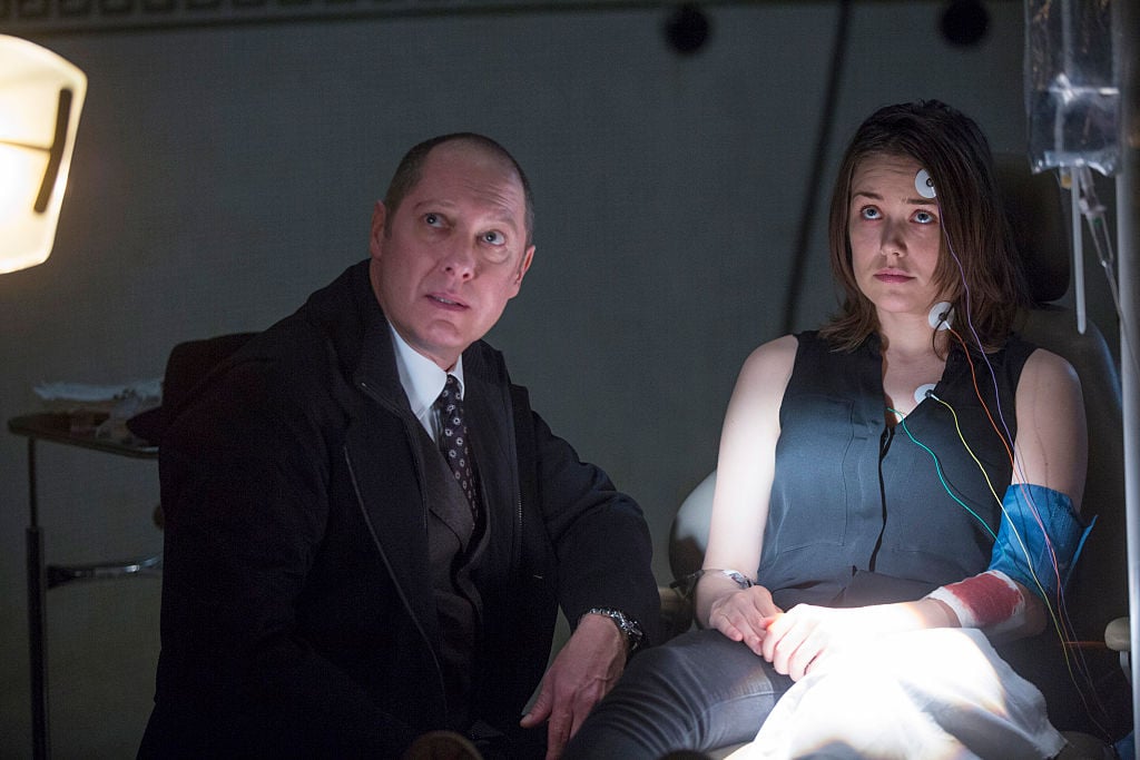 James Spader as Raymond 'Red' Reddington sits next to Megan Boone as Liz Keen while she's hooked up to a medical device.