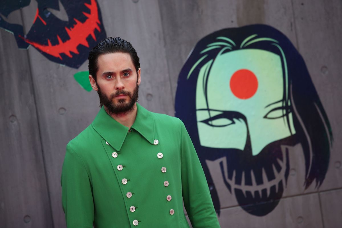 Jared Leto poses in a suit in front of ‘Suicide Squad’ artwork