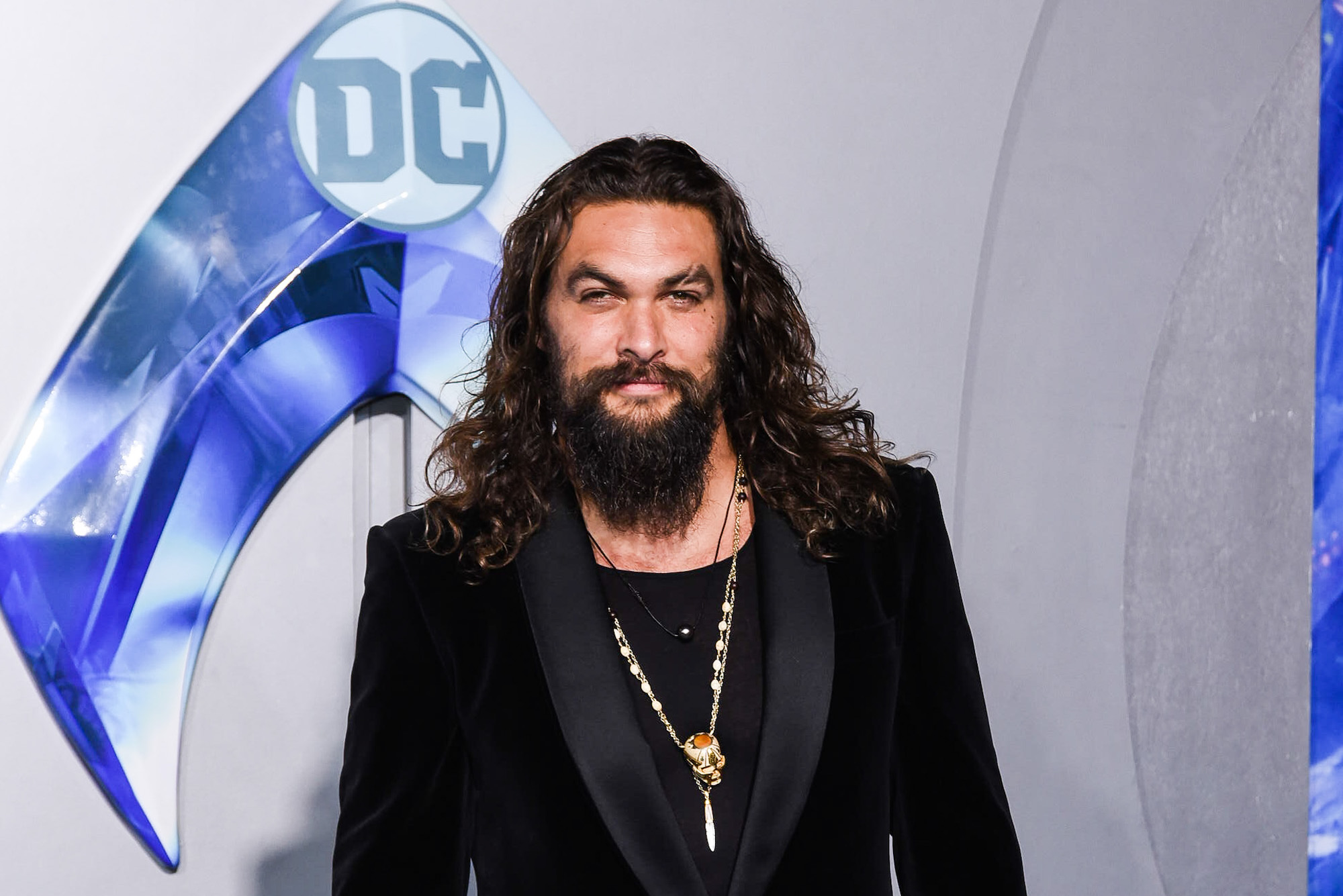 Jason Momoa smiling in front of a white background