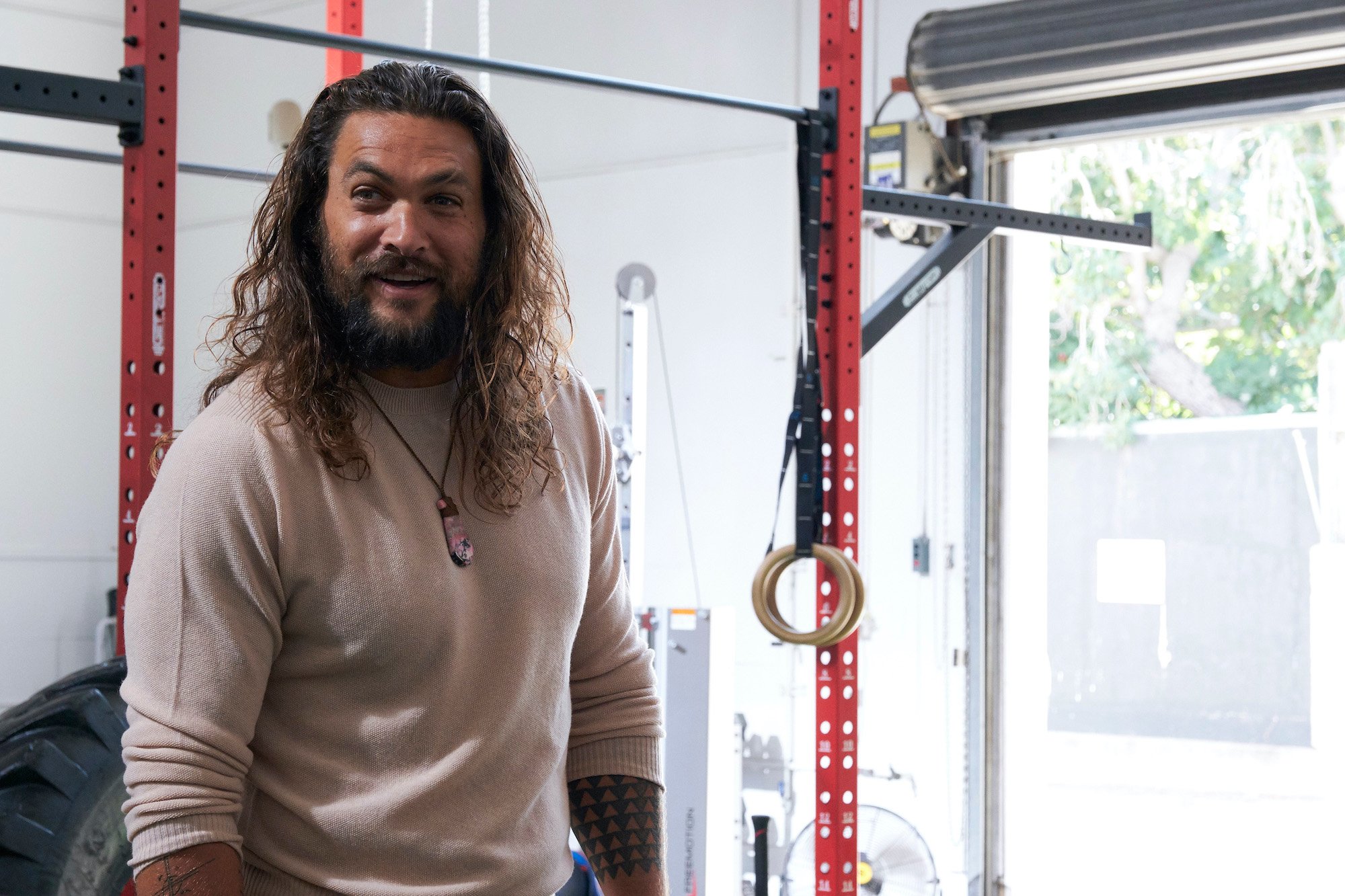 Jason Momoa smiling in front of exercise equipment