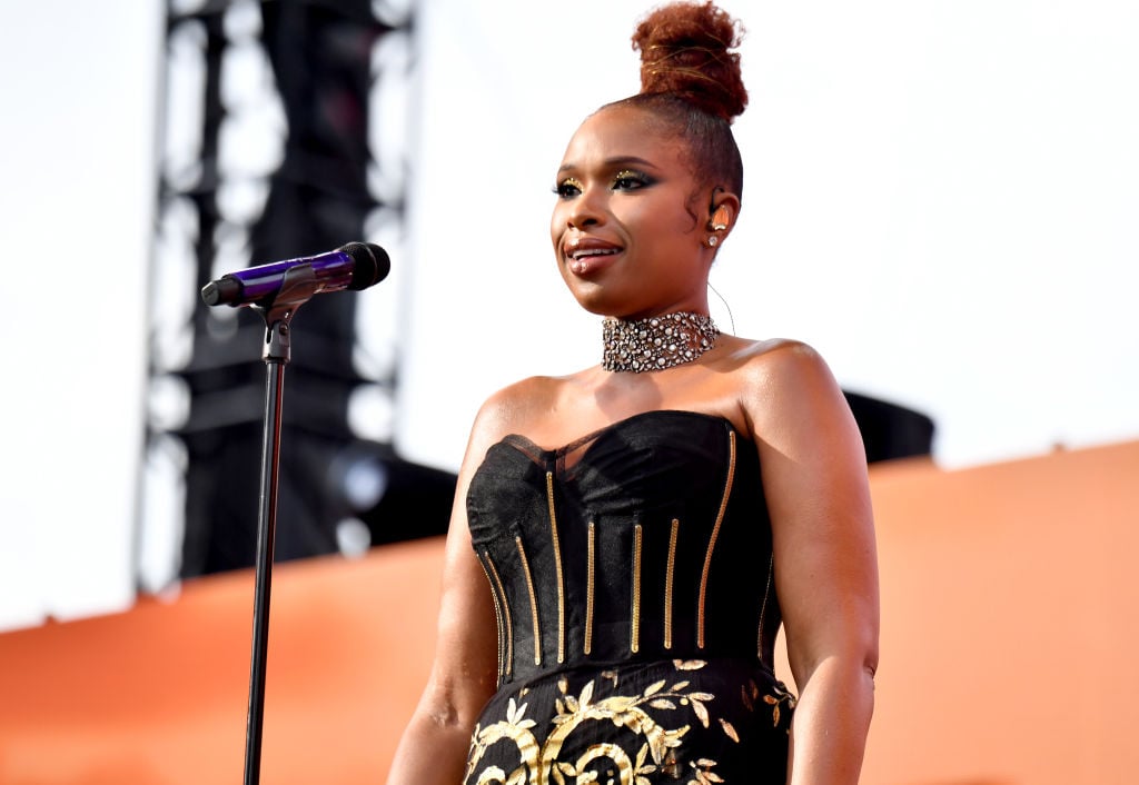 Jennifer Hudson sings on stage wearing a strapless, beaded, black gown that's embellished with gold.