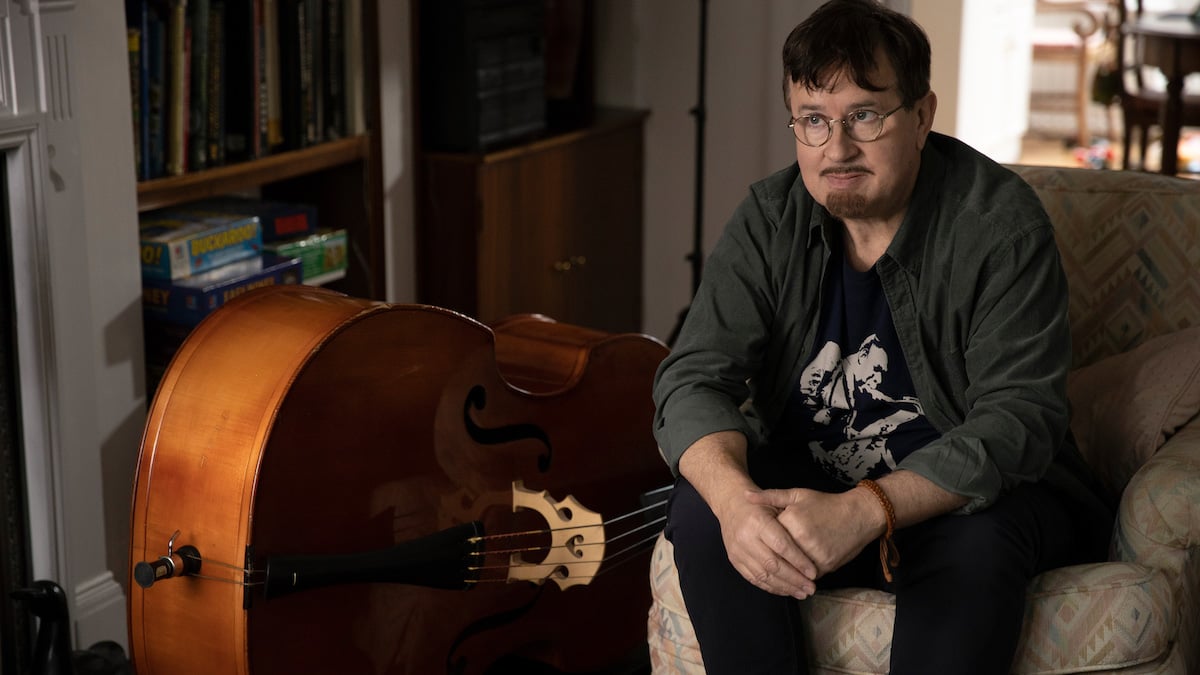 Jeremy Swift sits on a chair next to a double bass as Leslie Higgins in 'Ted Lasso'