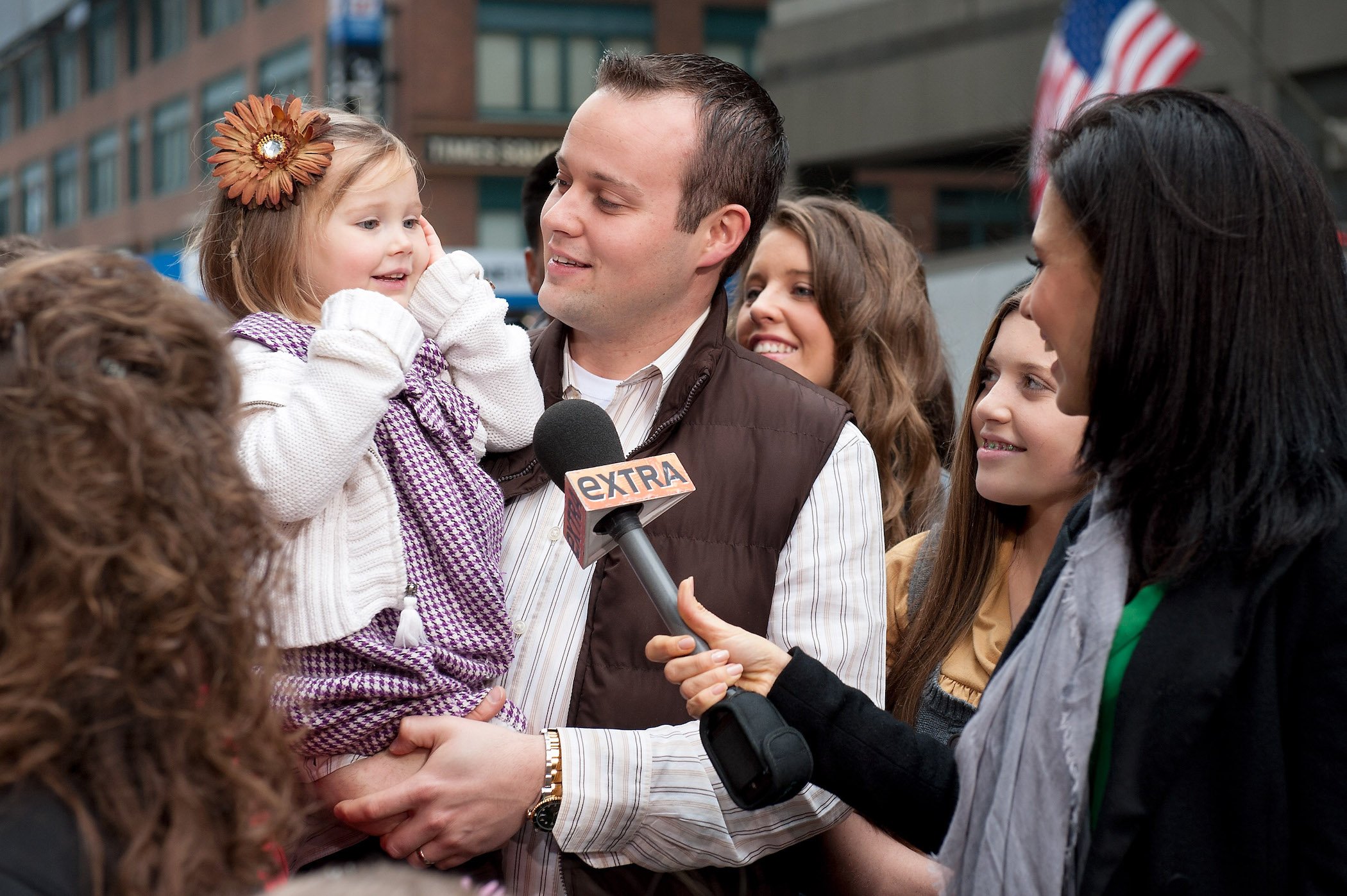 Josh Duggar of the Duggar family holding his young daughter with the other Duggars around him during an interview