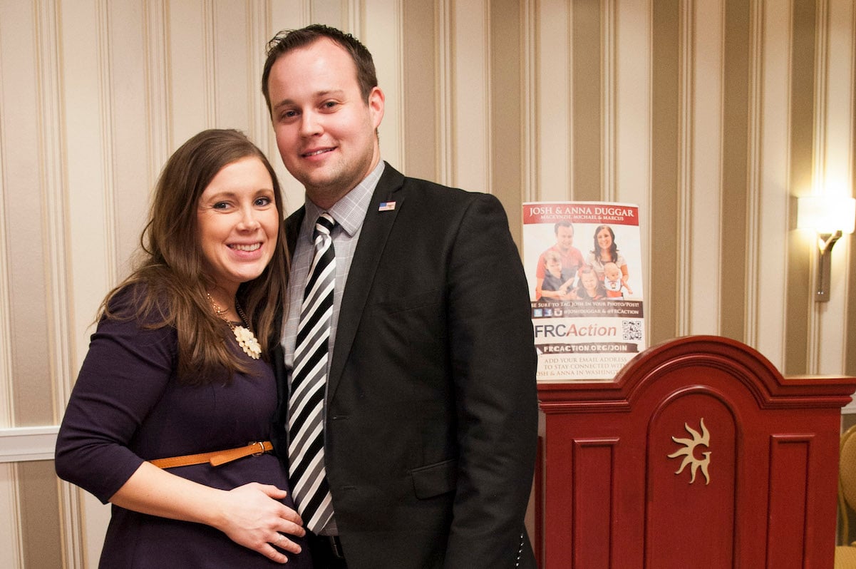 Anna Duggar wearing a blue dress posing for a photo with her husband Josh Duggar wearing a suit and tie.