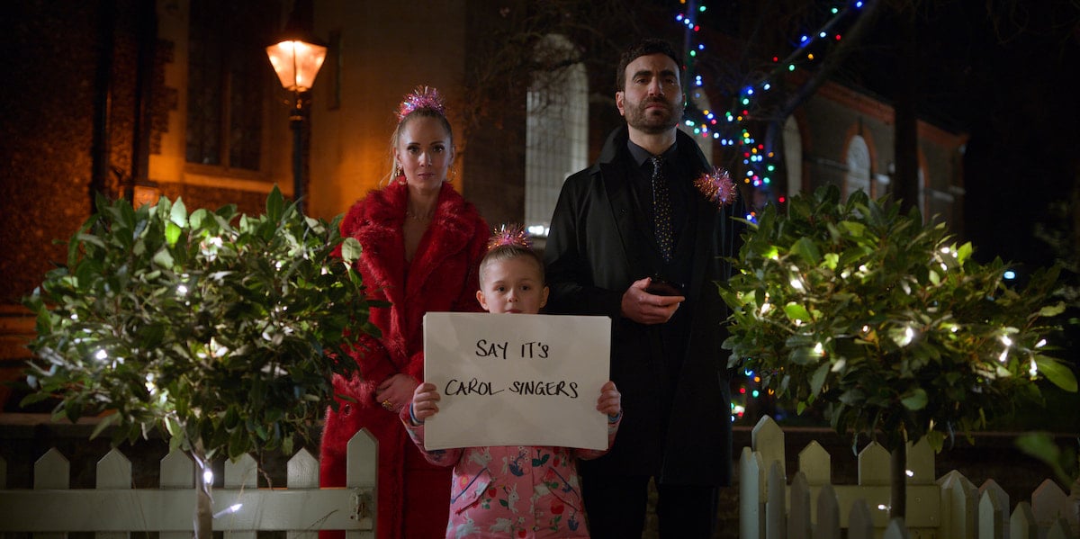 Juno Temple and Brett Goldstein stand between Elodie Blomfield as she holds up a poster board with writing on it in 'Ted Lasso' Season 2