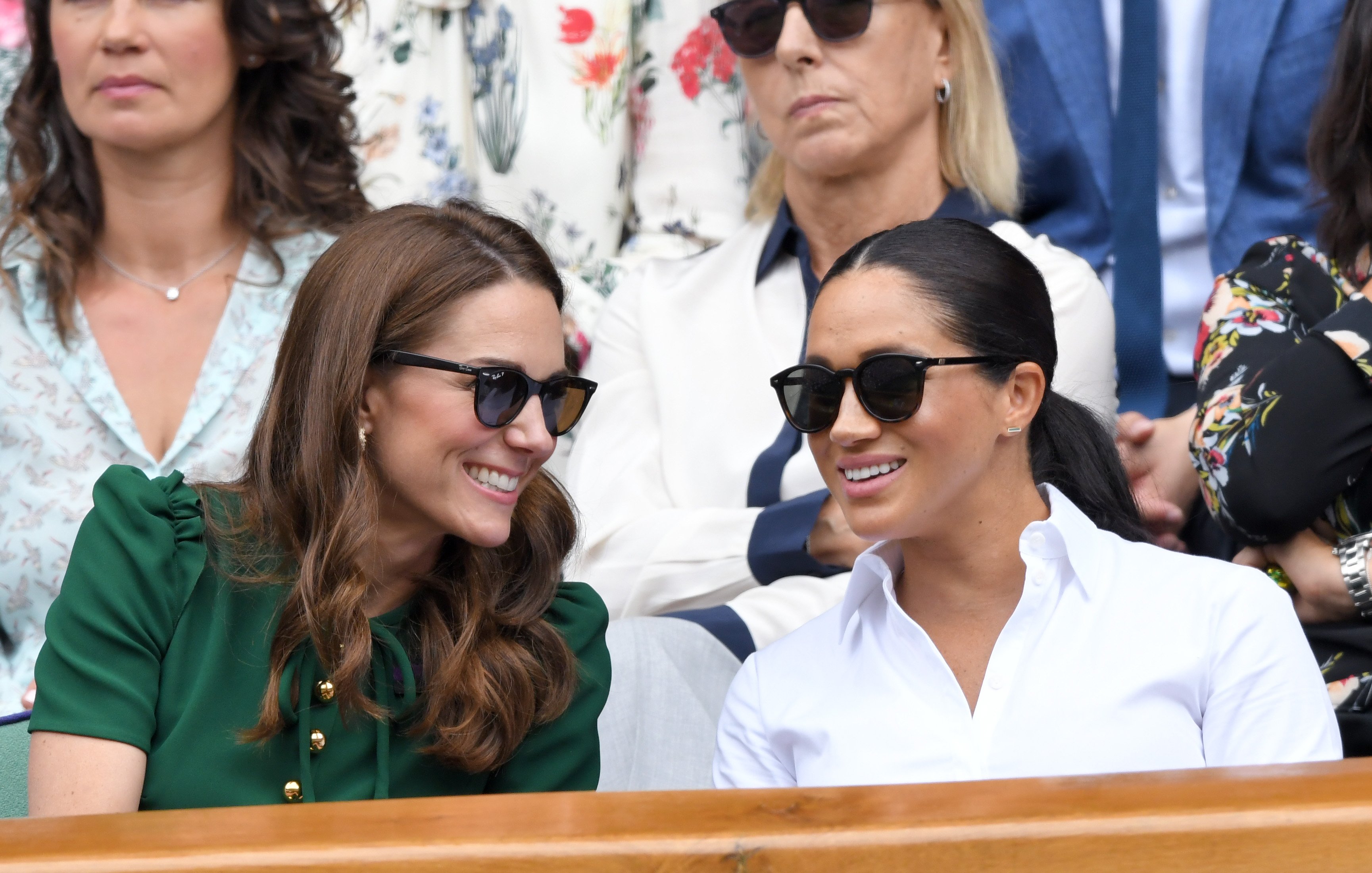 Kate Middleton in green dress and shades talking to Meghan Markle in white dress