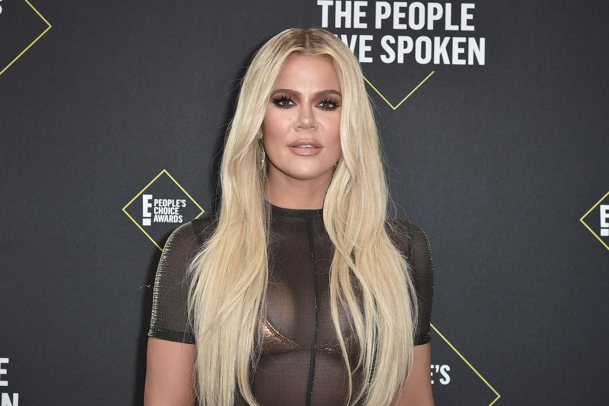 Khloe Kardashian with blonde hair, standing in front of dark background