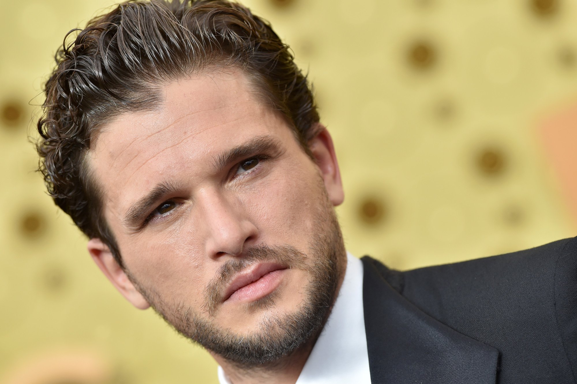 Game of Thrones star Kit Harington wearing a suit and standing in front of a golden wall
