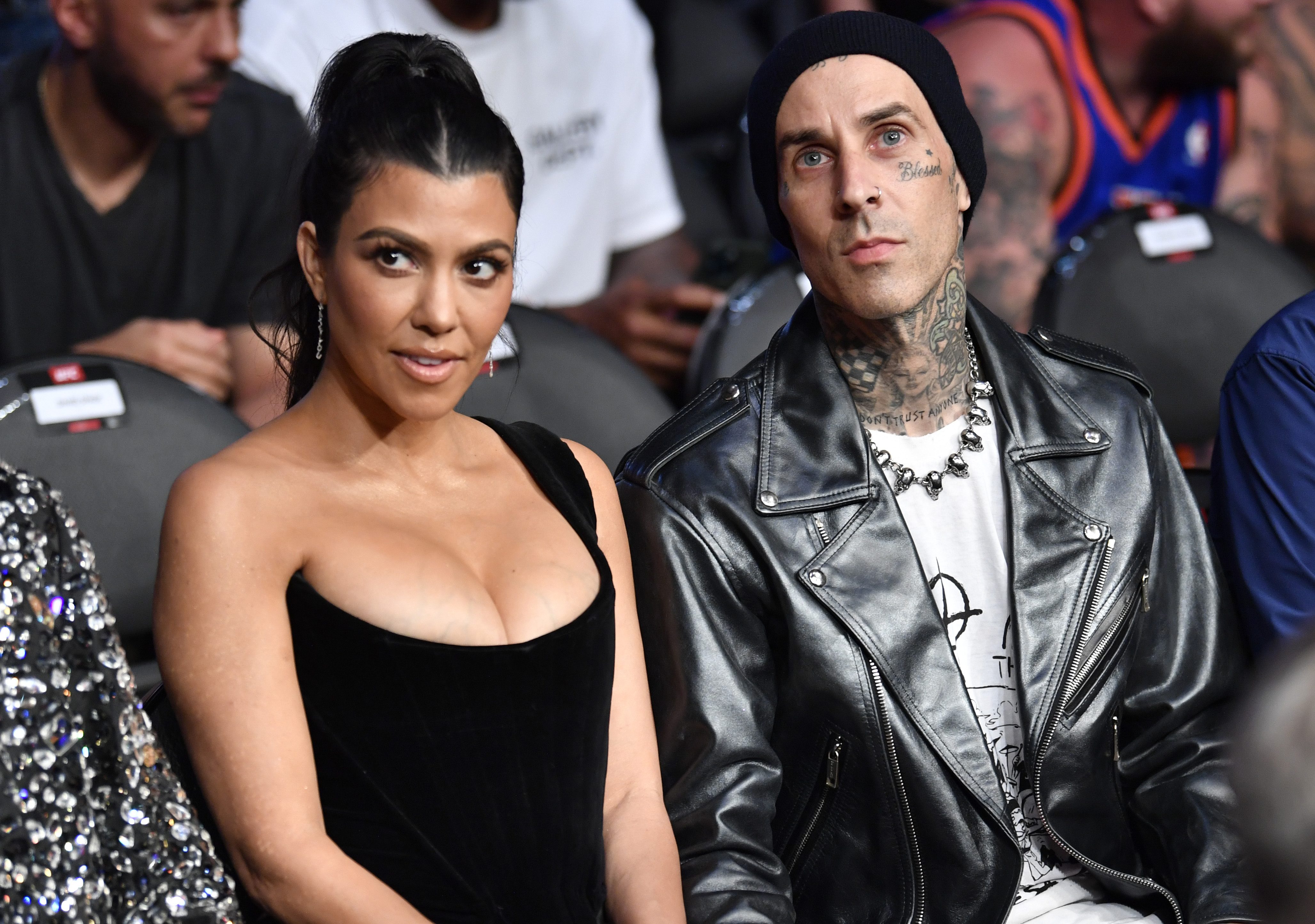 Kourtney Kardashian and Travis Barker sit side by side attending an event