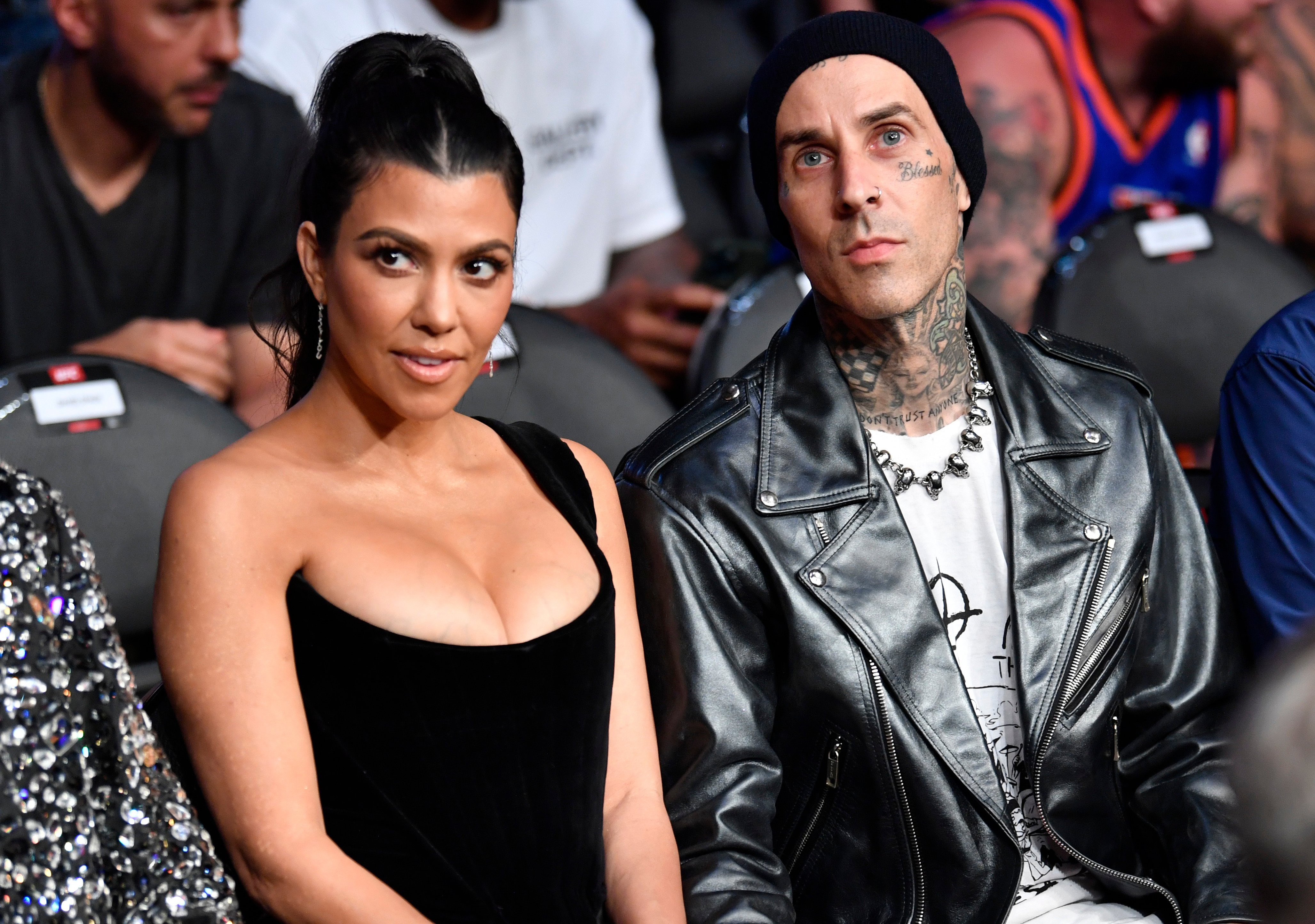 Kourtney Kardashian and Travis Barker sit side by side attending an event